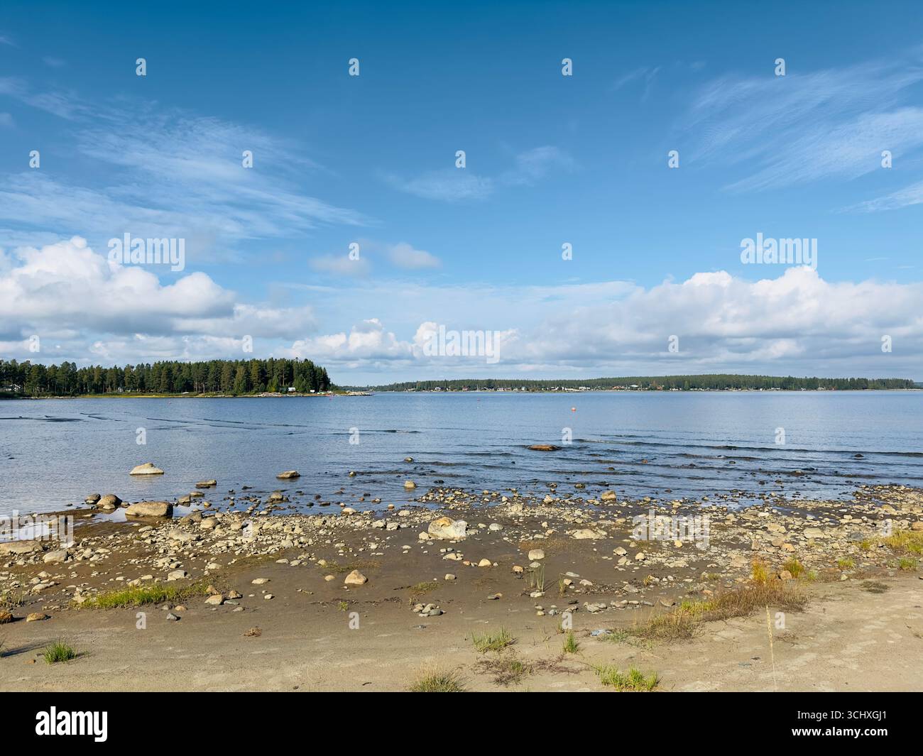 Scenic view of a rocky shoreline and calm water under a blue sky. - Smartphone Captured Stock Image