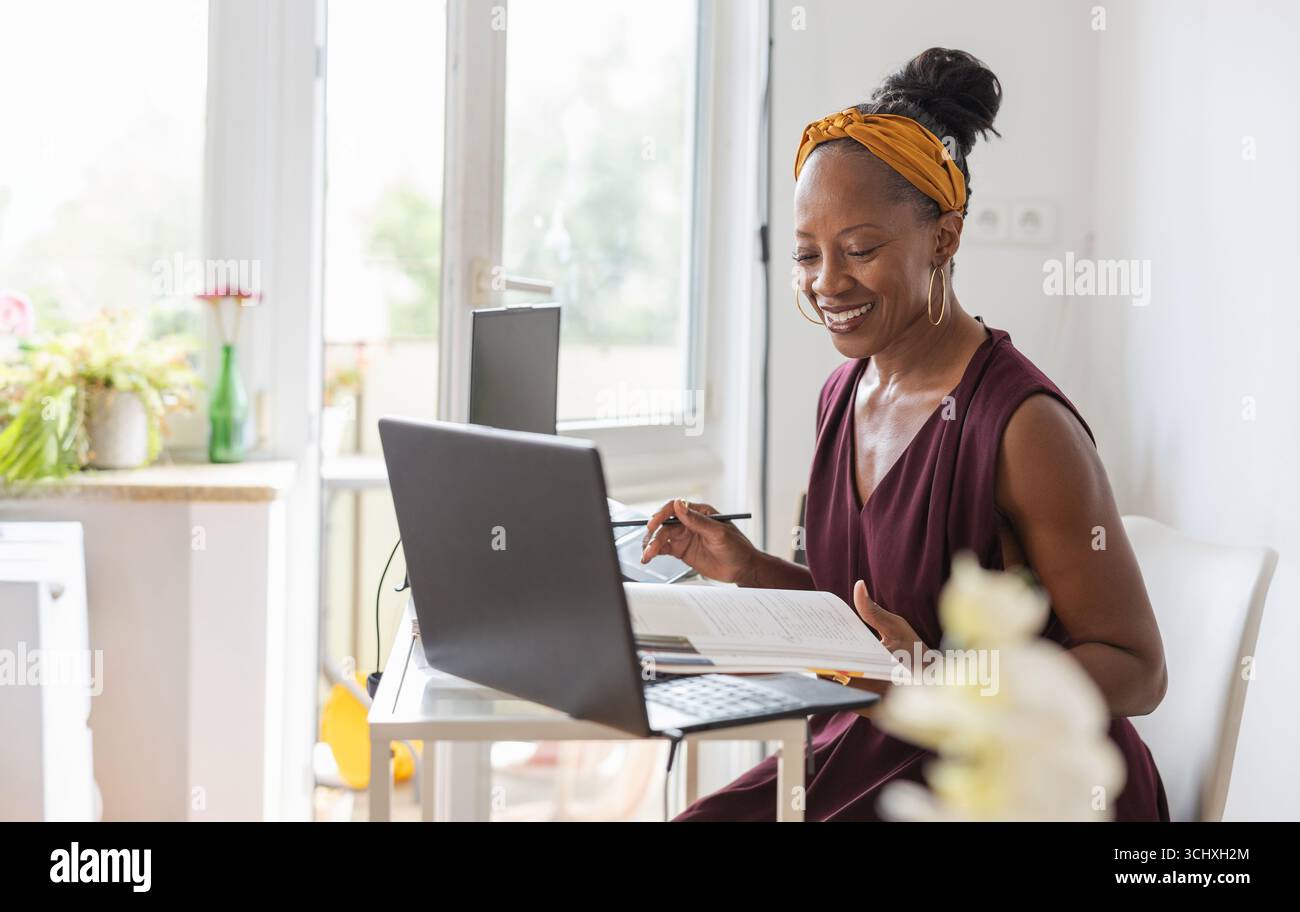 Smiling woman using laptop while sitting at desk in office Stock Photo