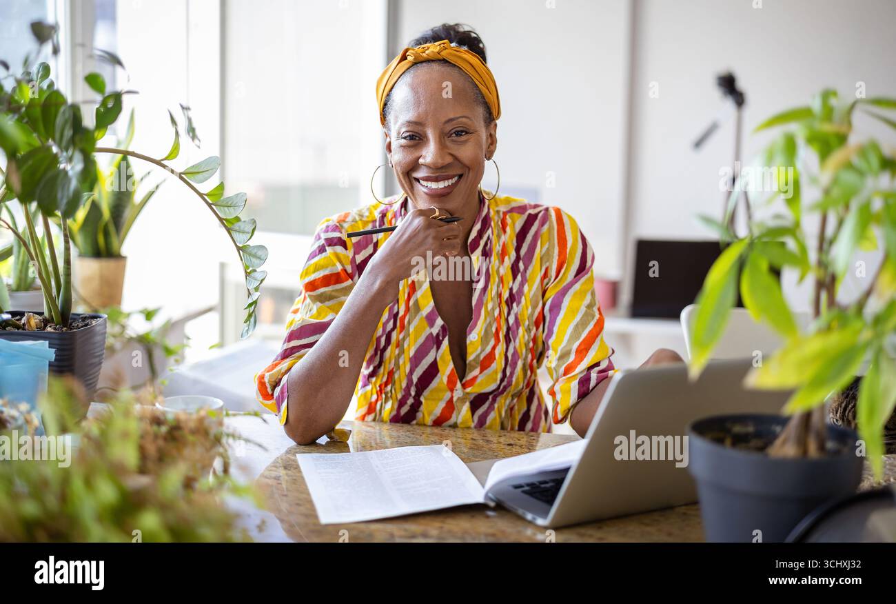 Smiling woman using laptop while sitting at desk in office Stock Photo