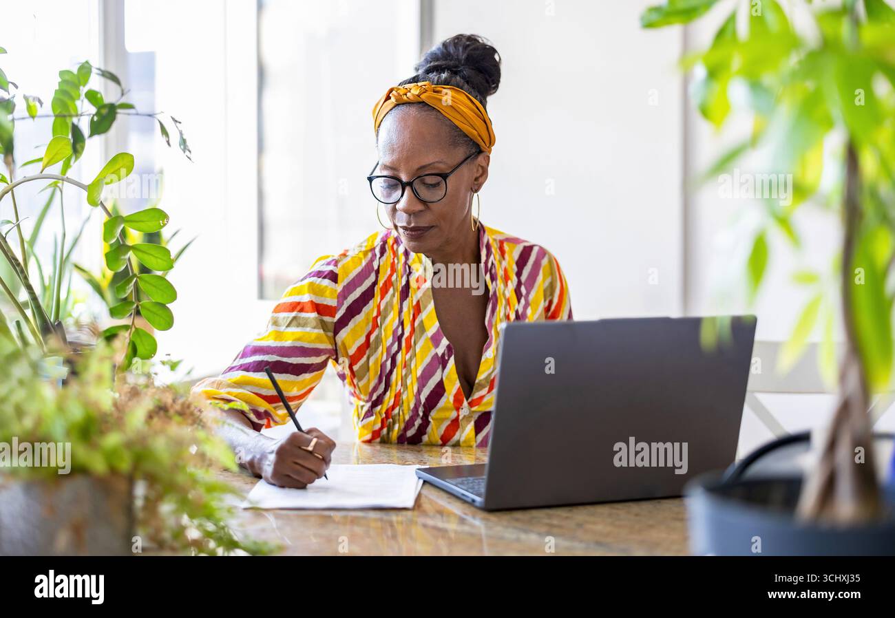 Portrait of confident businesswoman writing notes while using laptop in office Stock Photo