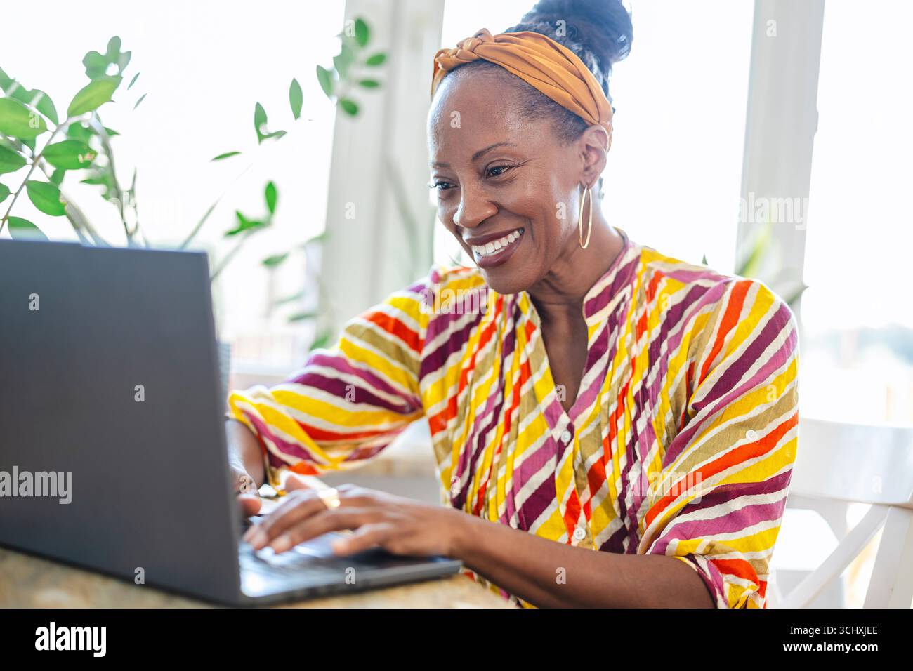 Smiling woman using laptop while sitting at desk in office Stock Photo
