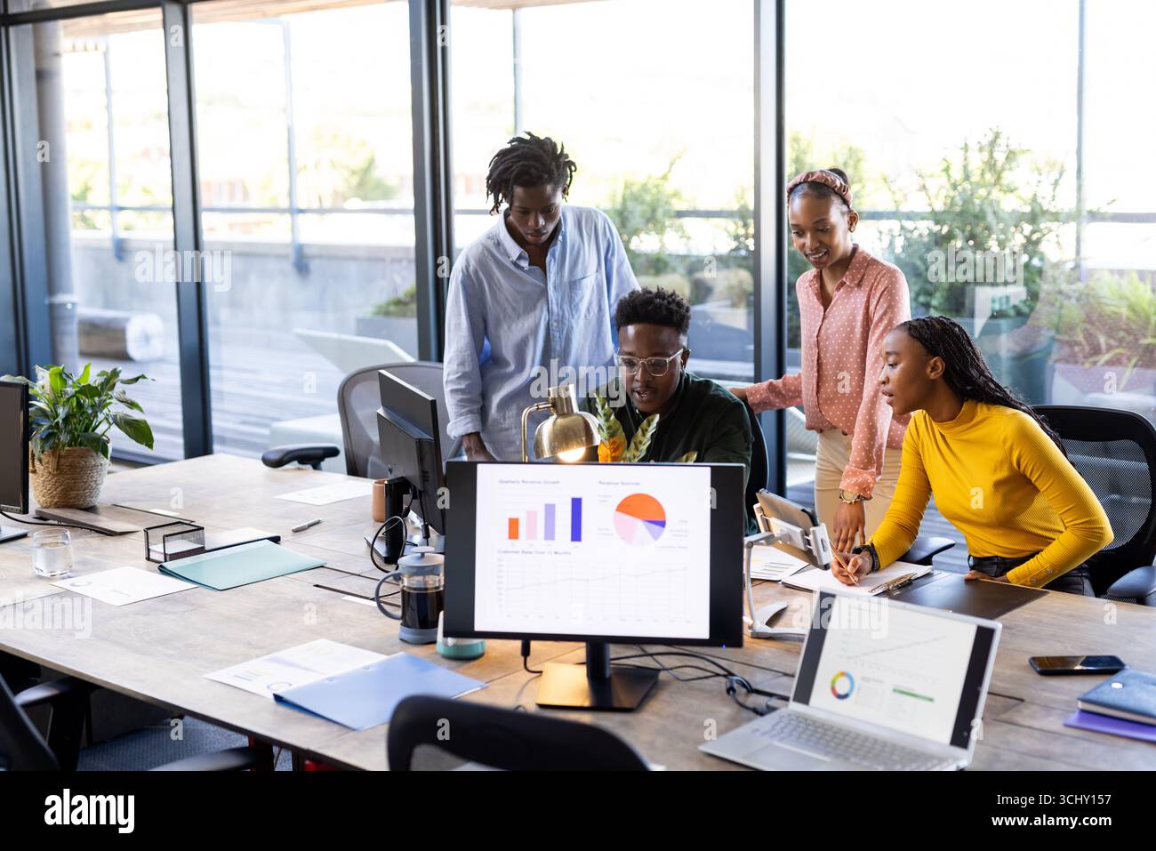Team collaborating on project, analyzing data on computer screens in modern office Stock Photo