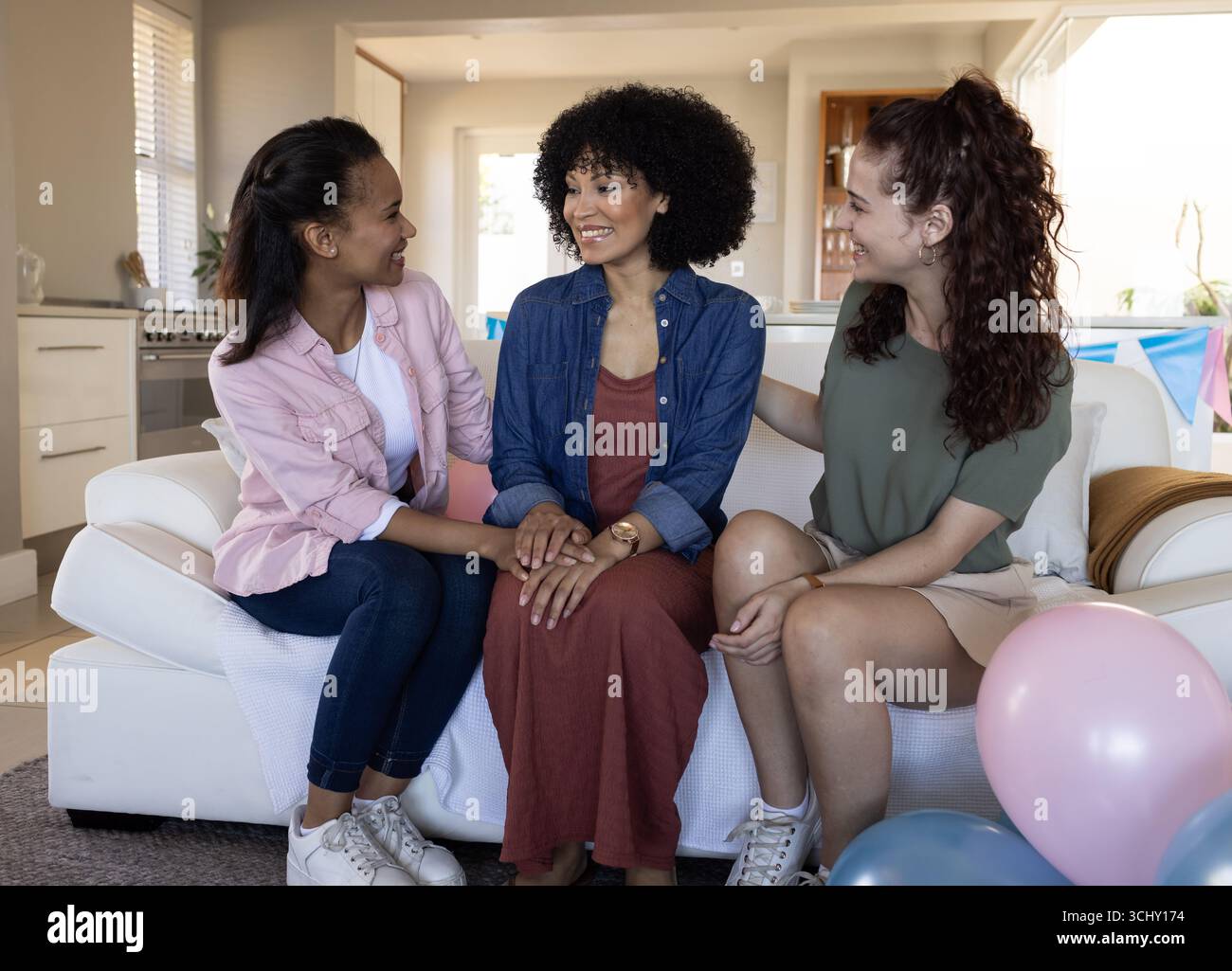 Three diverse female friends sitting on couch, smiling and celebrating friendship at home Stock Photo