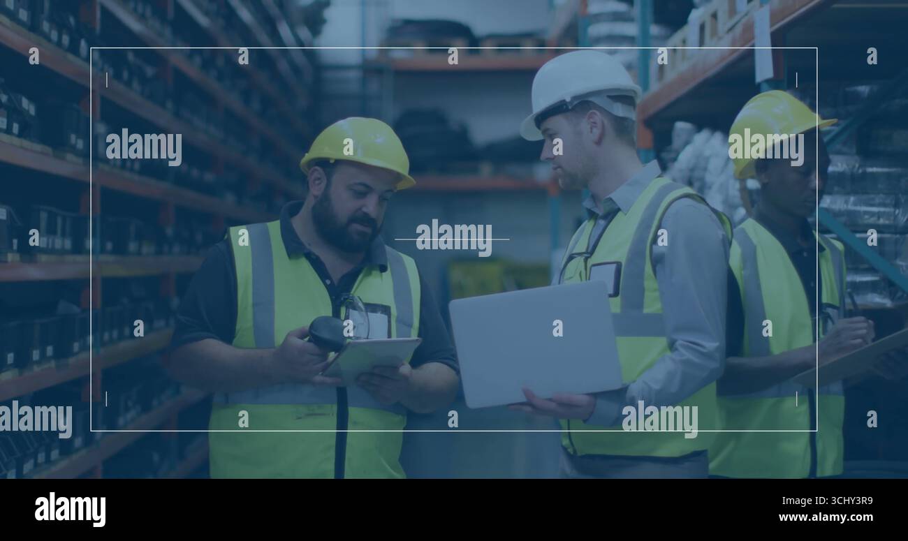 Workers in vests and helmets scanning inventory using scanner, checking on tablet in storage aisle Stock Photo