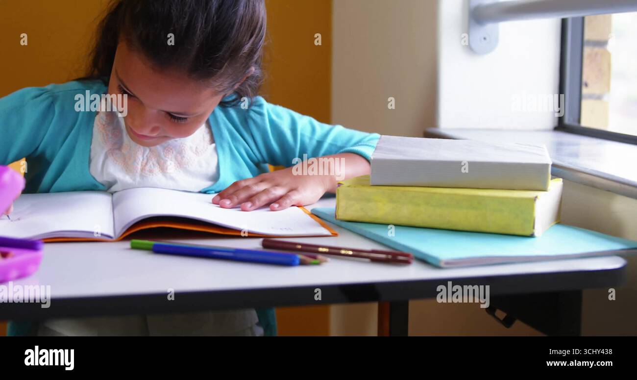 Leaning student in turquoise cardigan writing in open notebook at study nook by window, copy space Stock Photo