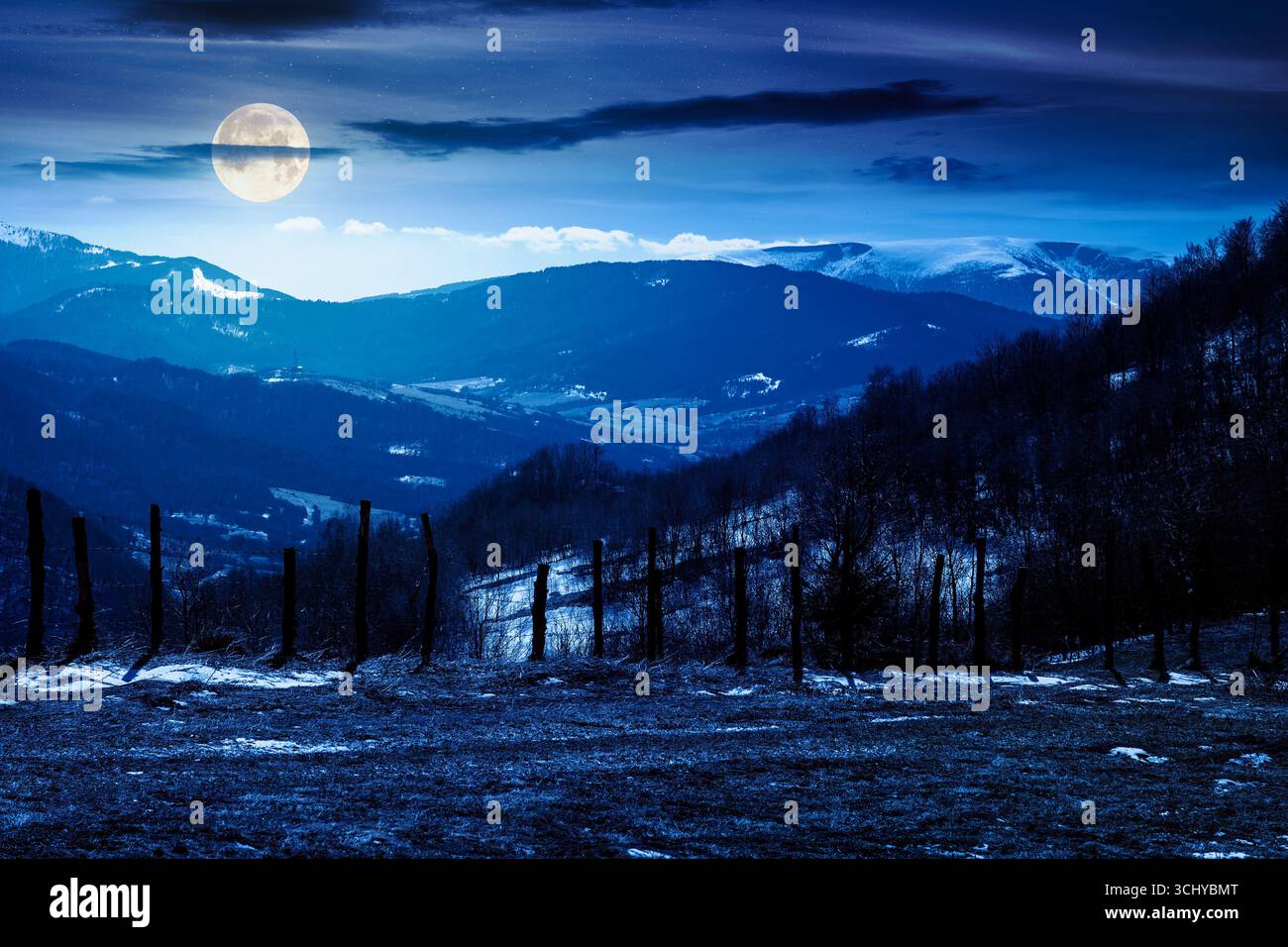 mountainous countryside at night. winter to spring season change scenery. melting snow and leafless trees on the rolling hills in full moon light. vie Stock Photo