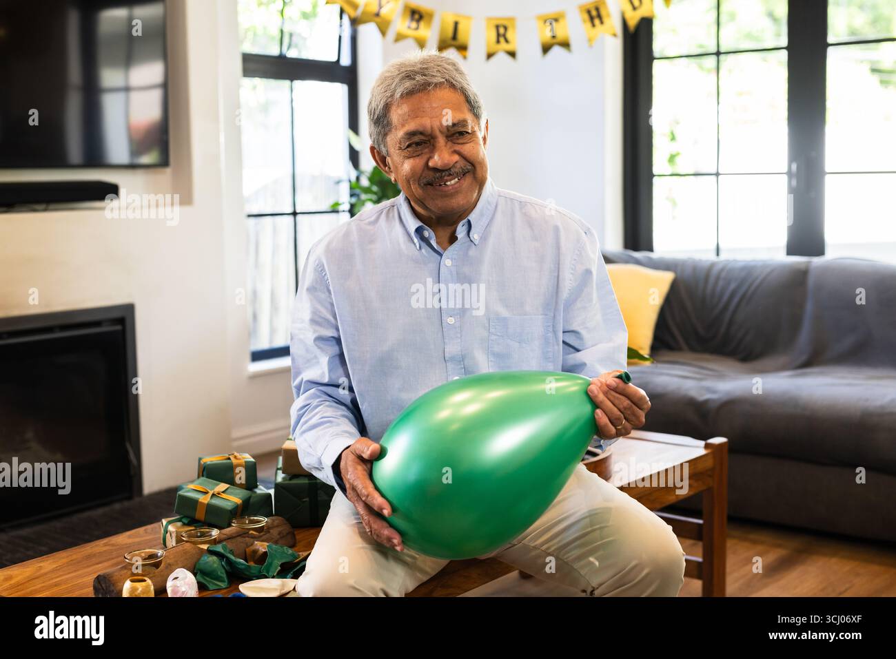 Smiling senior man inflating green balloon at home birthday celebration ...