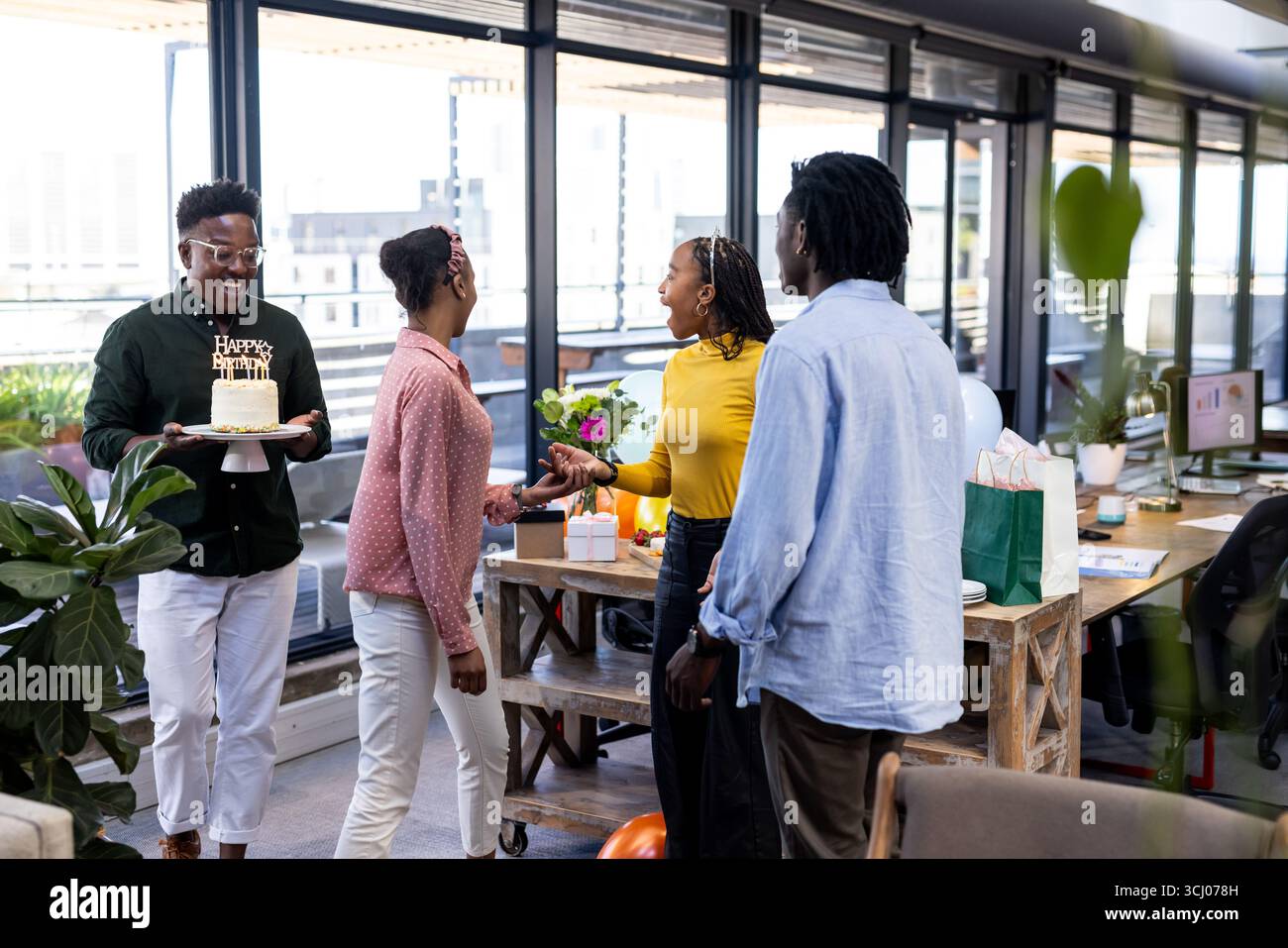 Celebrating birthday in office, colleagues with cake and flowers, smiling happily Stock Photo