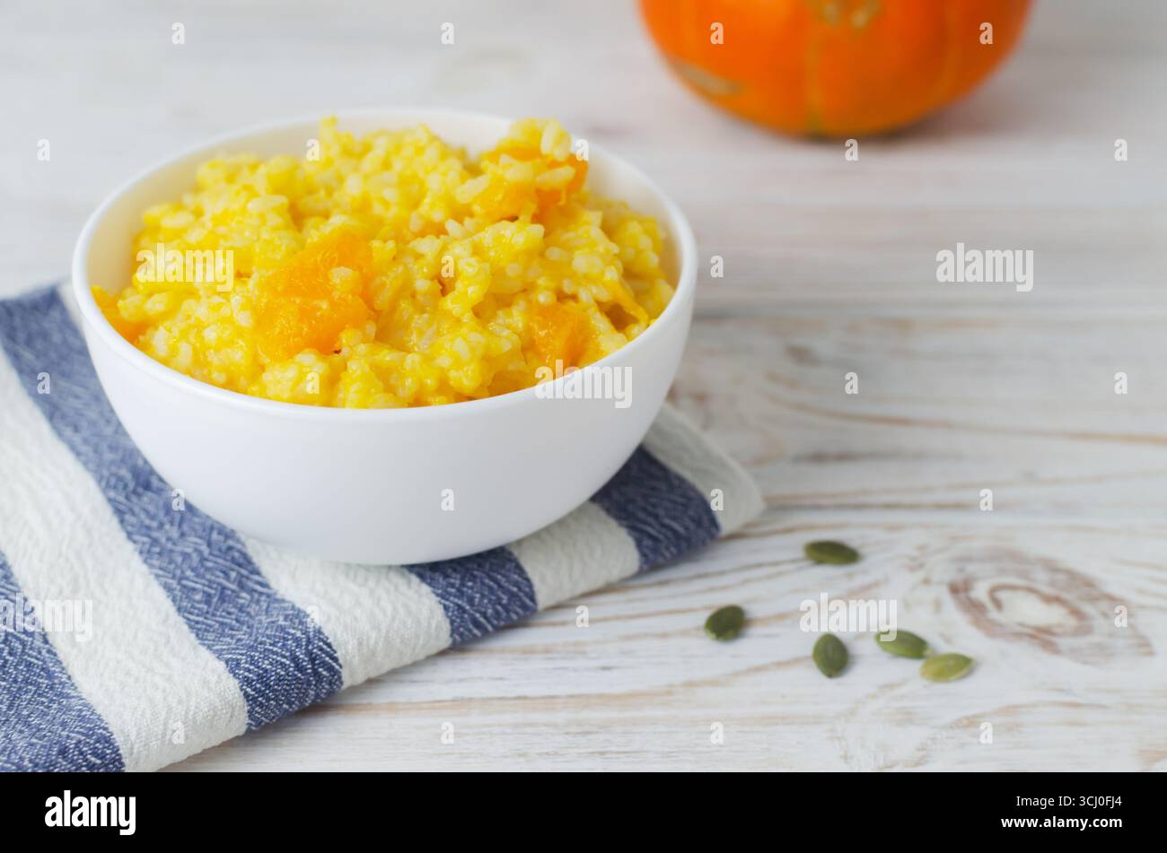 Pumpkin risotto in a white bowl on a striped napkin on a wooden table. Italian dish concept. Autumn food. Selective focus. Horizontal orientation. Cop Stock Photo