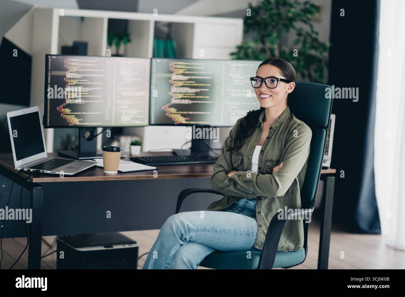 Professional software developer working remotely in her stylish home office with dual monitors showcasing programming code Stock Photo