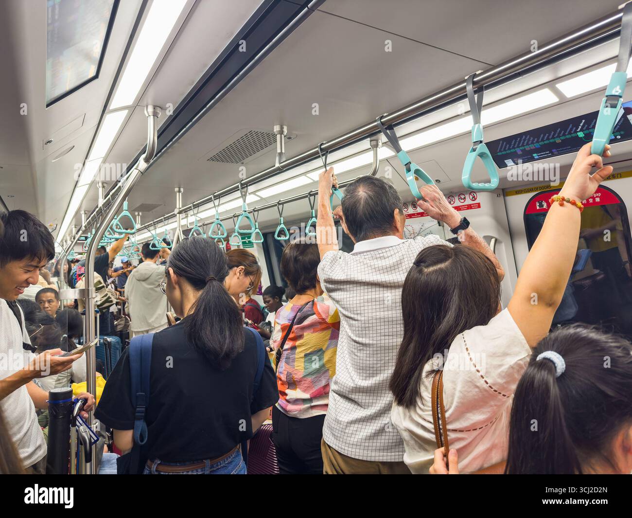 A crowded subway train with standing passengers holding onto handrails during a busy commute in an urban environment singapore MRT asia - Smartphone Captured Stock Image
