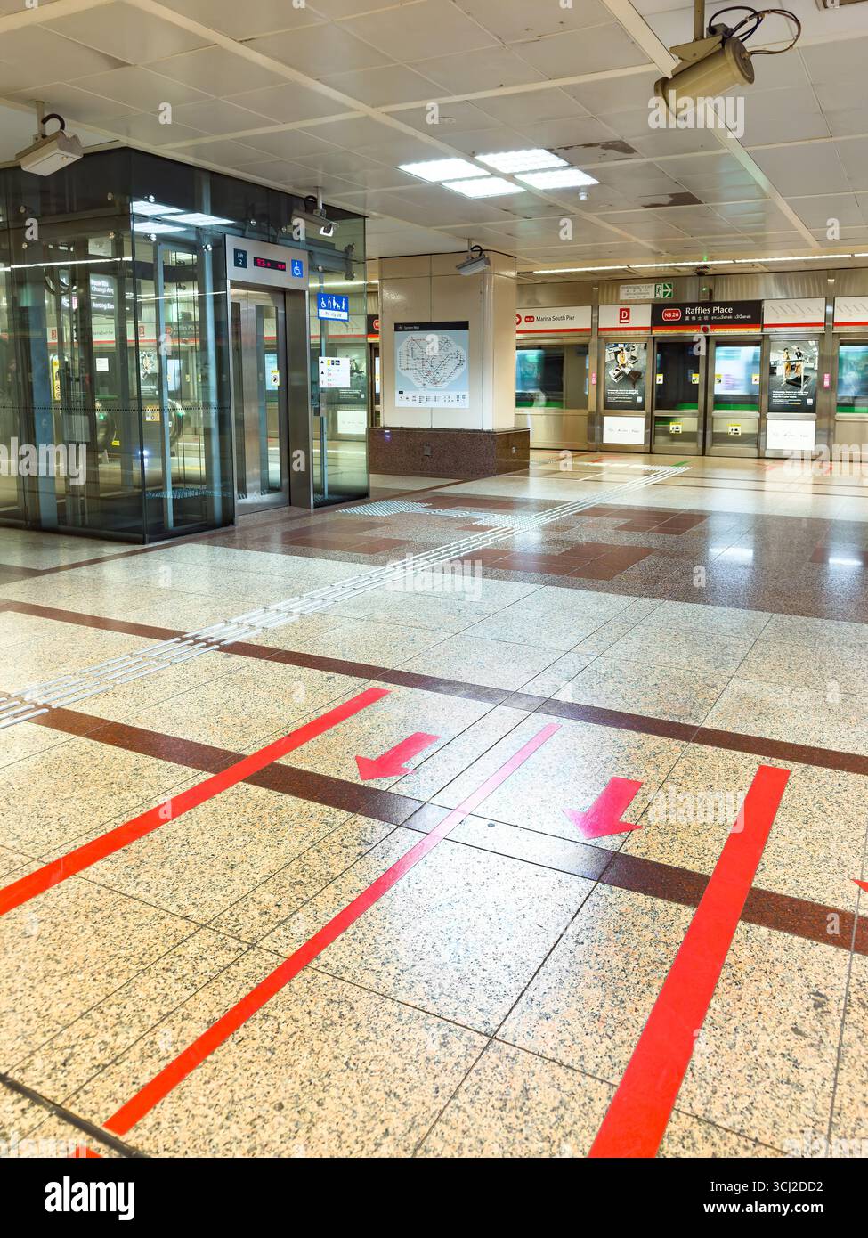 Empty interior of a modern subway station with red directional arrows on the floor and a glass elevator nearby Raffles Place Singapore MRT - Smartphone Captured Stock Image