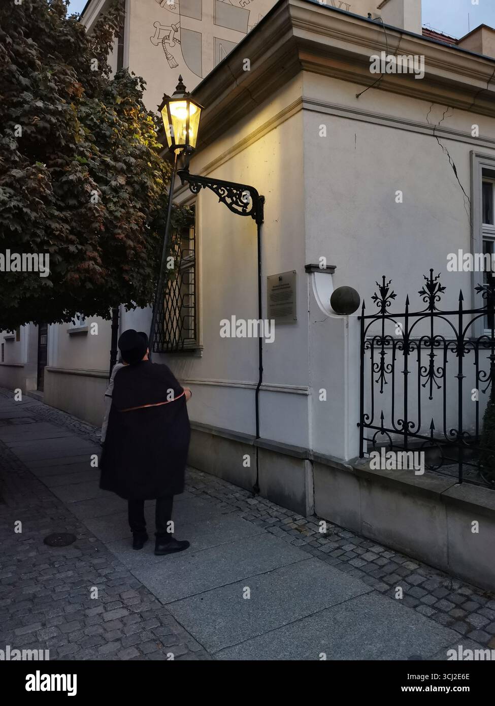 Wrocław lamplighter in hat and cloak lighting gas lamps on Cathedral Island at dusk—historic tradition, Poland, tourism, street scene, Ostrów Tumski. - Smartphone Captured Stock Image