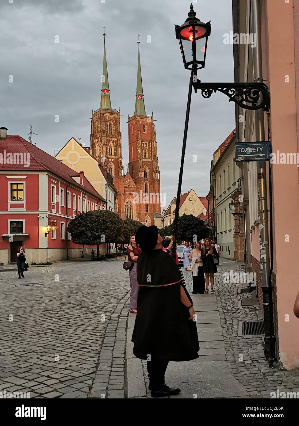 Wrocław lamplighter in hat and cloak lighting gas lamps on Cathedral Island at dusk—historic tradition, Poland, tourism, street scene, Ostrów Tumski. - Smartphone Captured Stock Image