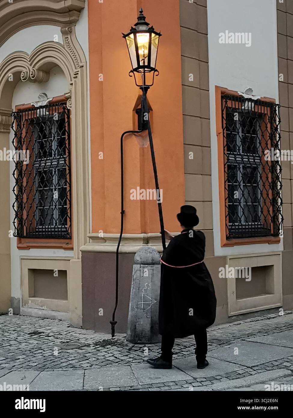 Wrocław lamplighter in hat and cloak lighting gas lamps on Cathedral Island at dusk—historic tradition, Poland, tourism, street scene, Ostrów Tumski. - Smartphone Captured Stock Image