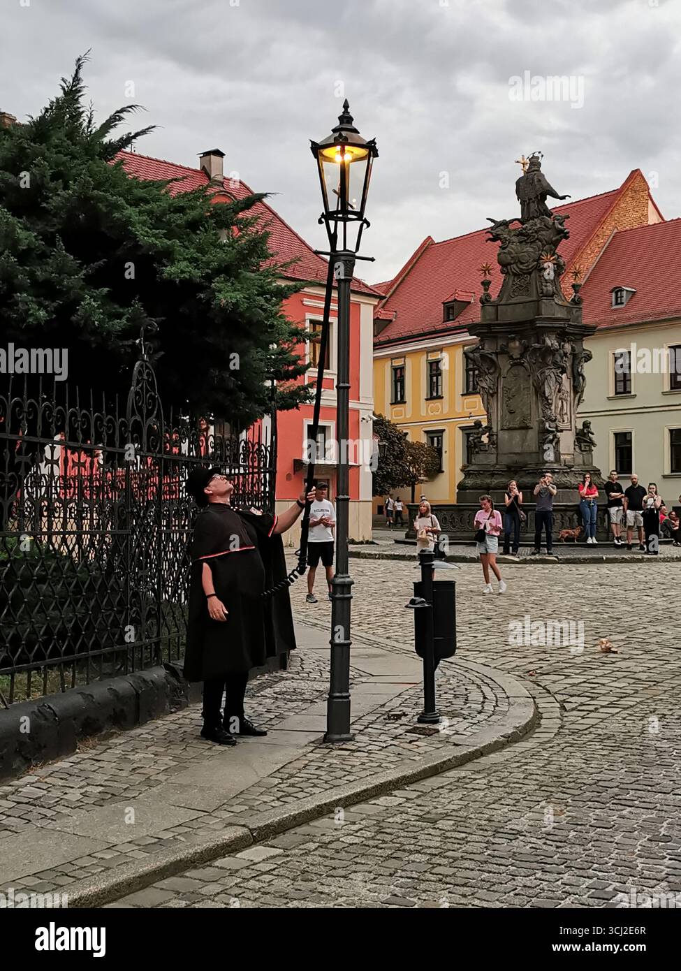 Wrocław lamplighter in hat and cloak lighting gas lamps on Cathedral Island at dusk—historic tradition, Poland, tourism, street scene, Ostrów Tumski. - Smartphone Captured Stock Image