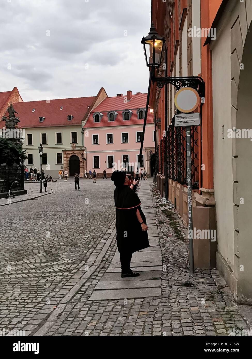Wrocław lamplighter in hat and cloak lighting gas lamps on Cathedral Island at dusk—historic tradition, Poland, tourism, street scene, Ostrów Tumski. - Smartphone Captured Stock Image