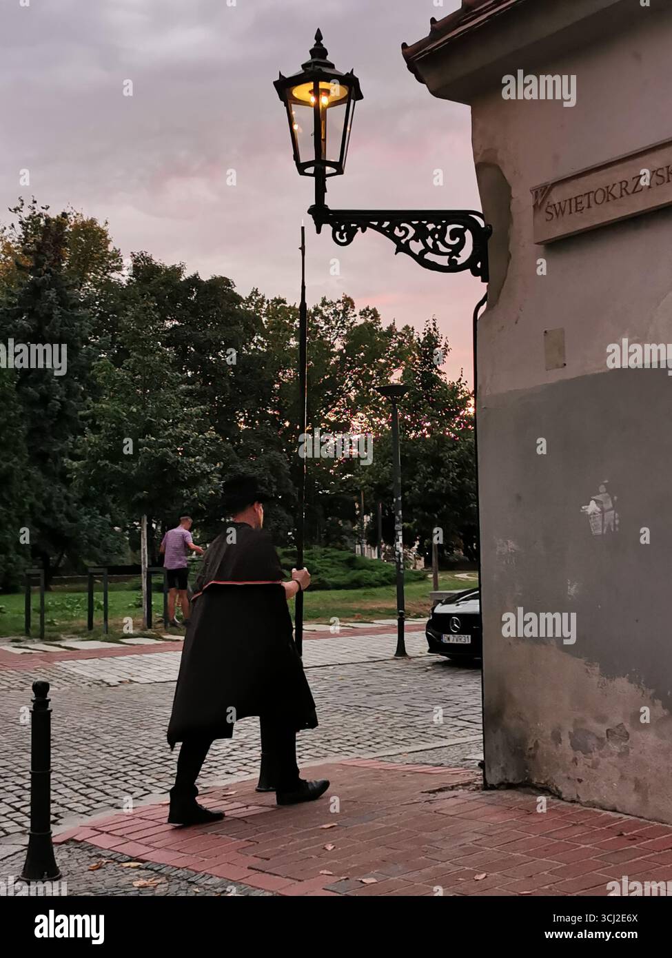 Wrocław lamplighter in hat and cloak lighting gas lamps on Cathedral Island at dusk—historic tradition, Poland, tourism, street scene, Ostrów Tumski. - Smartphone Captured Stock Image
