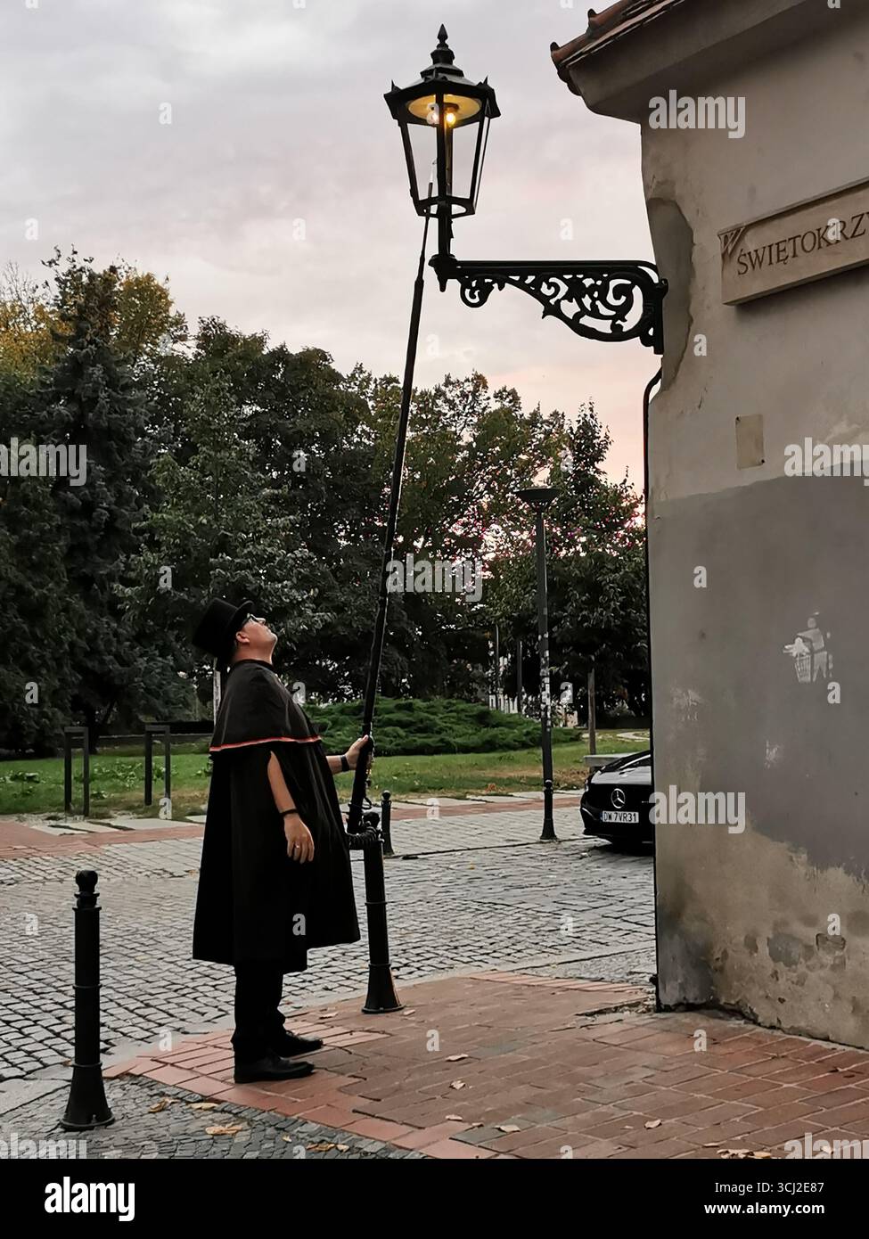 Wrocław lamplighter in hat and cloak lighting gas lamps on Cathedral Island at dusk—historic tradition, Poland, tourism, street scene, Ostrów Tumski. - Smartphone Captured Stock Image