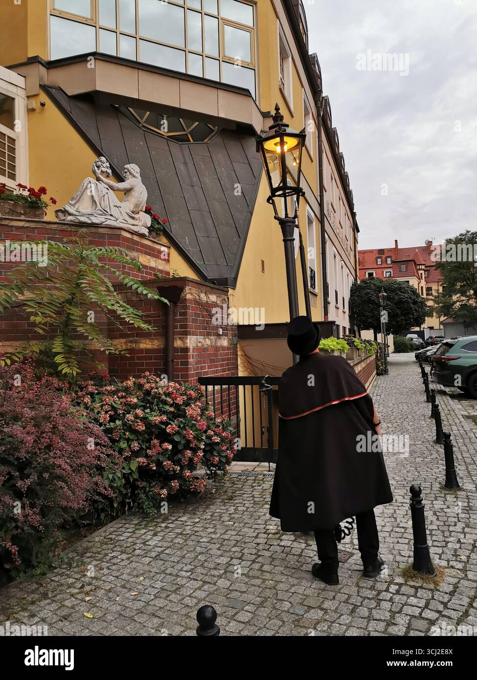 Wrocław lamplighter in hat and cloak lighting gas lamps on Cathedral Island at dusk—historic tradition, Poland, tourism, street scene, Ostrów Tumski. - Smartphone Captured Stock Image