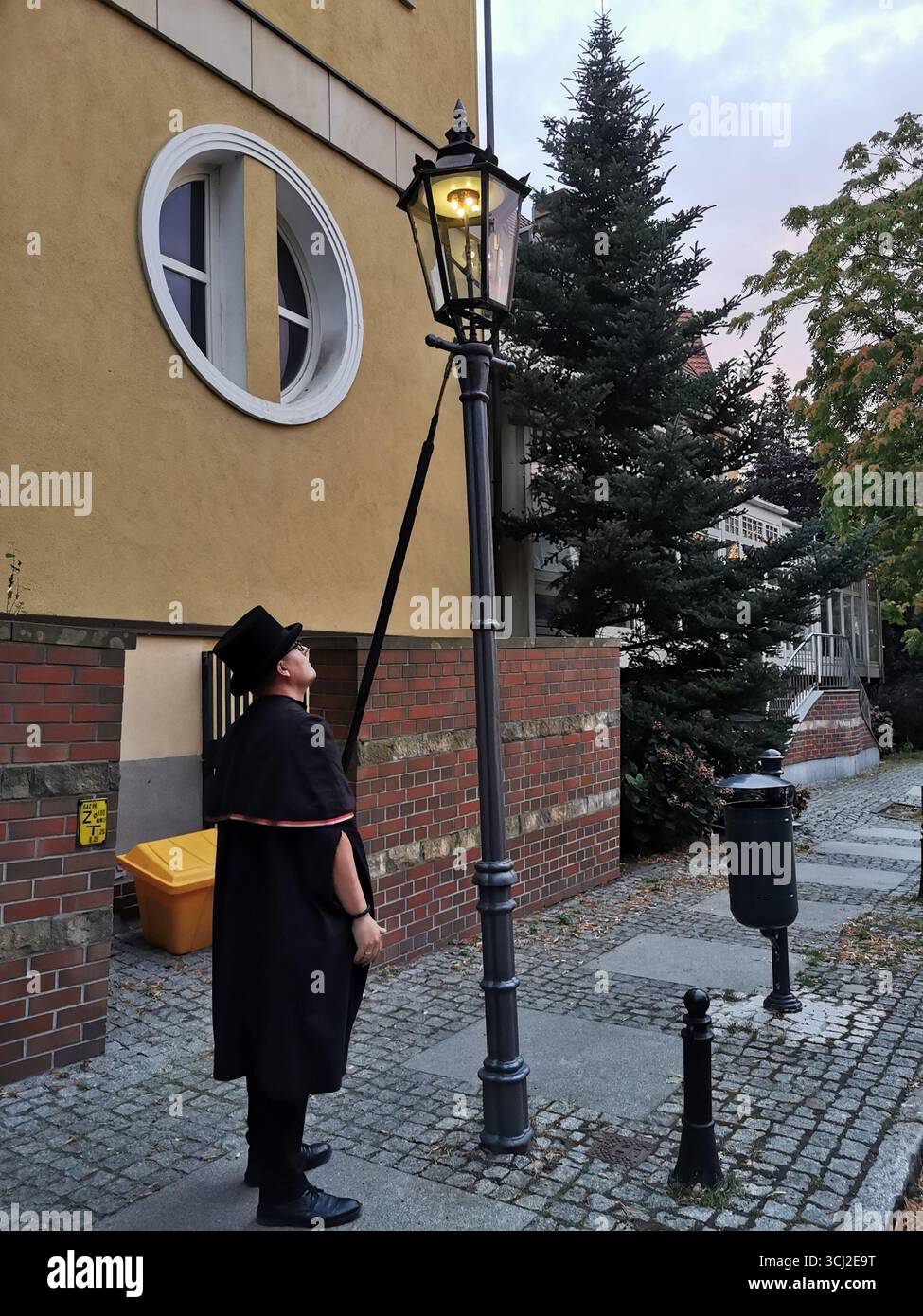 Wrocław lamplighter in hat and cloak lighting gas lamps on Cathedral Island at dusk—historic tradition, Poland, tourism, street scene, Ostrów Tumski. - Smartphone Captured Stock Image