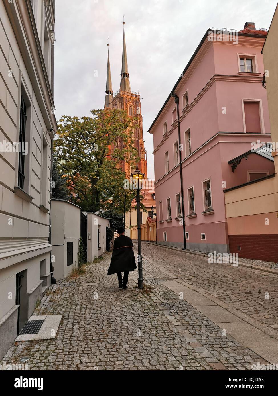 Wrocław lamplighter in hat and cloak lighting gas lamps on Cathedral Island at dusk—historic tradition, Poland, tourism, street scene, Ostrów Tumski. - Smartphone Captured Stock Image
