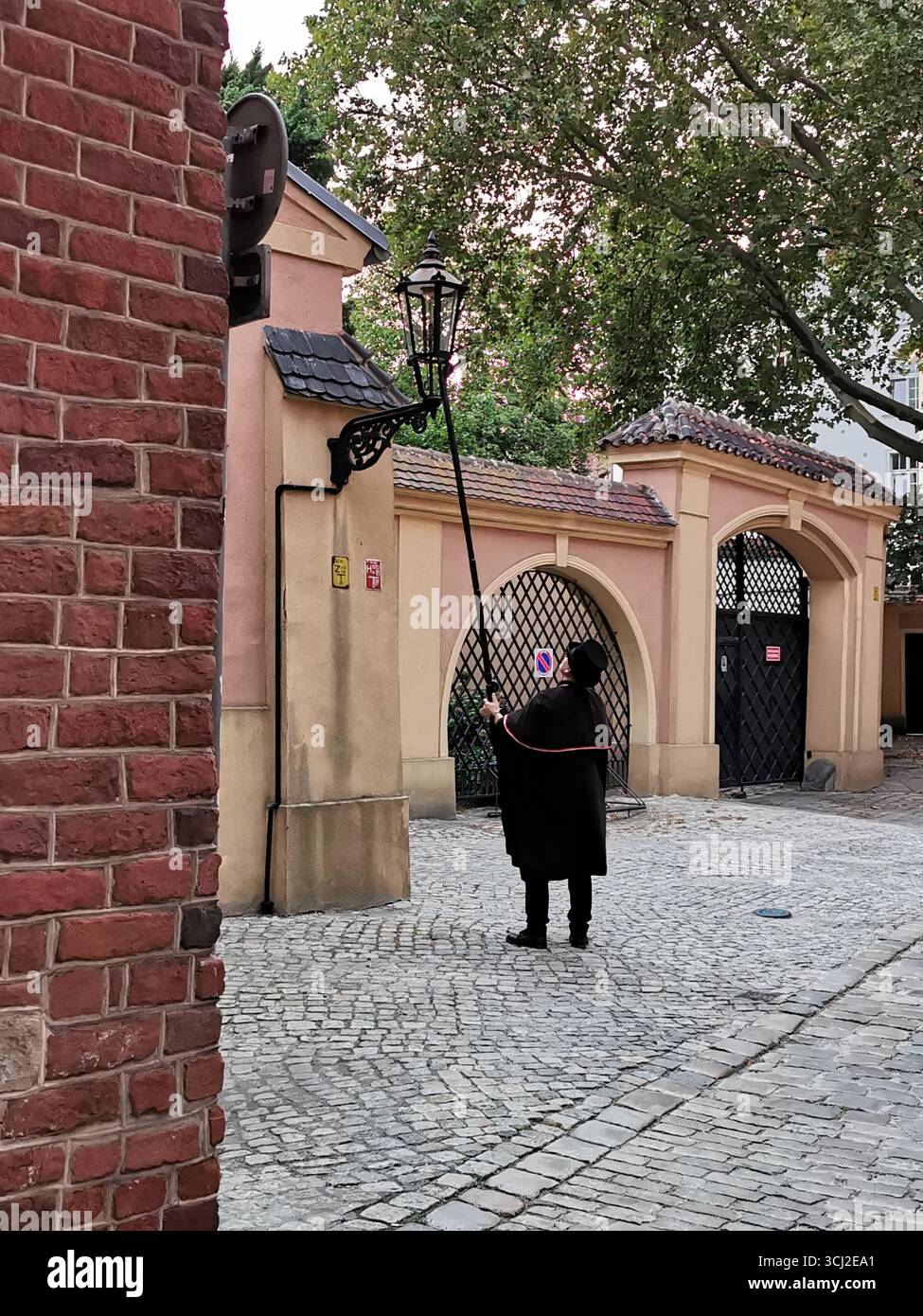 Wrocław lamplighter in hat and cloak lighting gas lamps on Cathedral Island at dusk—historic tradition, Poland, tourism, street scene, Ostrów Tumski. - Smartphone Captured Stock Image