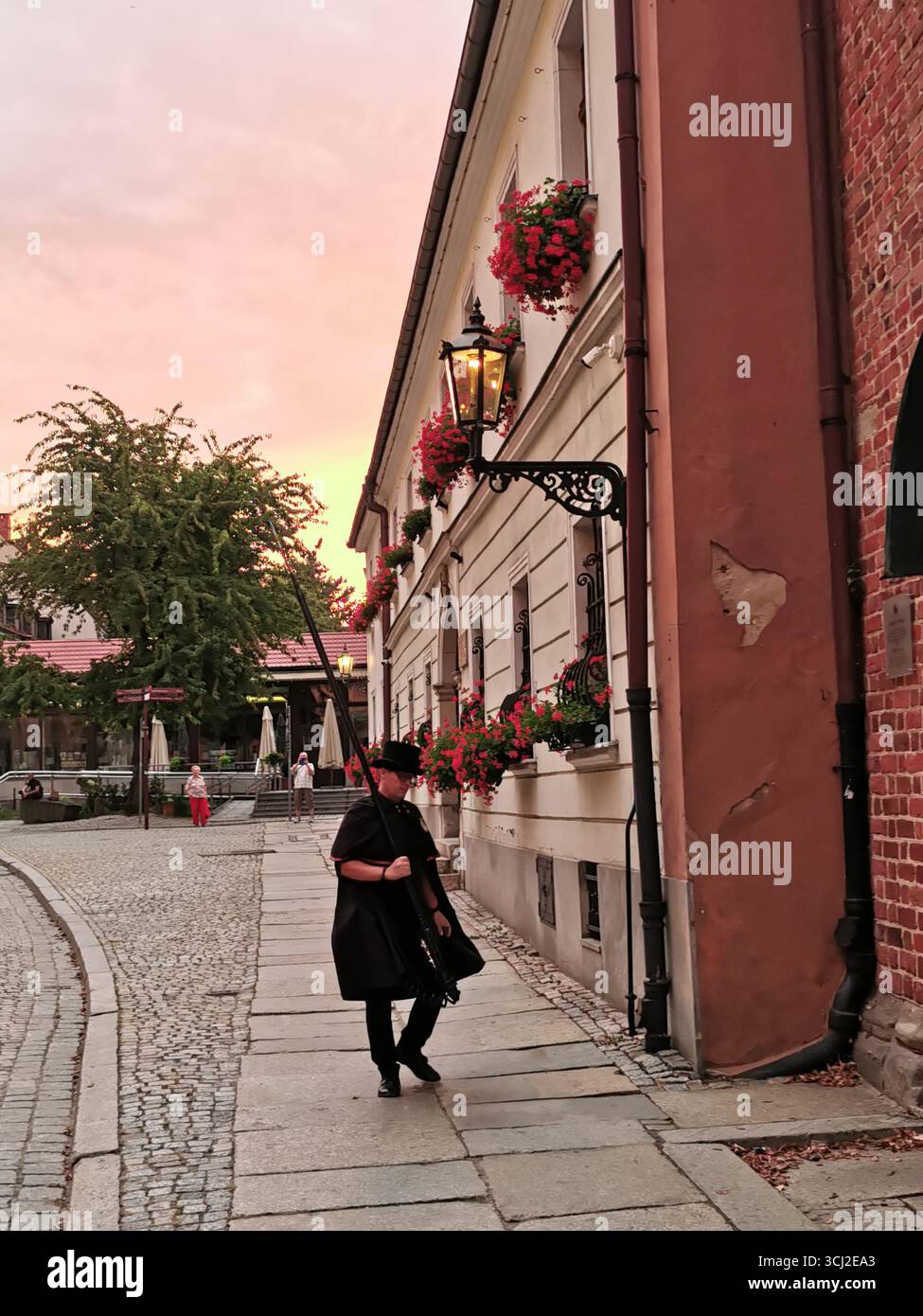 Wrocław lamplighter in hat and cloak lighting gas lamps on Cathedral Island at dusk—historic tradition, Poland, tourism, street scene, Ostrów Tumski. - Smartphone Captured Stock Image