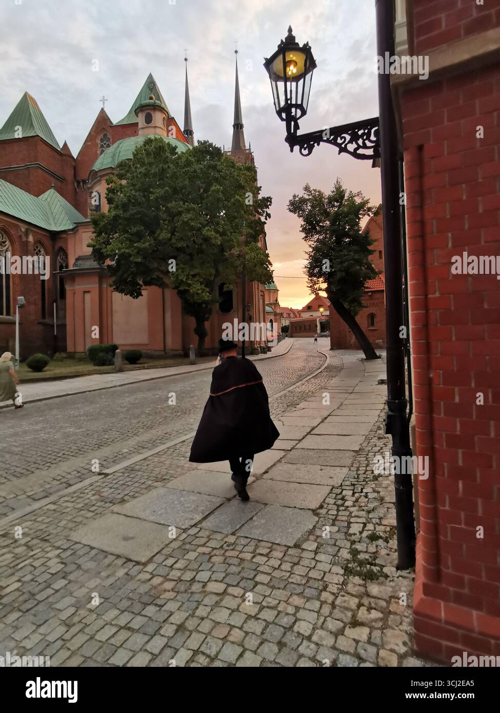 Wrocław lamplighter in hat and cloak lighting gas lamps on Cathedral Island at dusk—historic tradition, Poland, tourism, street scene, Ostrów Tumski. - Smartphone Captured Stock Image
