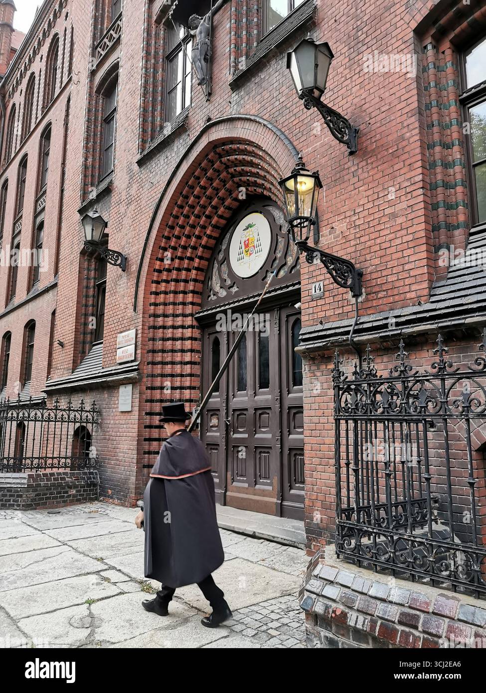 Wrocław lamplighter in hat and cloak lighting gas lamps on Cathedral Island at dusk—historic tradition, Poland, tourism, street scene, Ostrów Tumski. - Smartphone Captured Stock Image