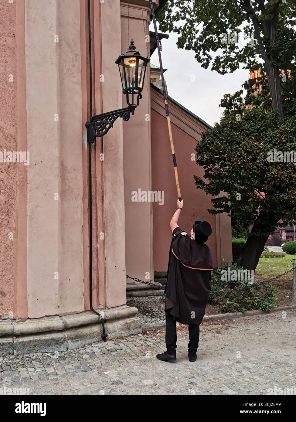 Wrocław lamplighter in hat and cloak lighting gas lamps on Cathedral Island at dusk—historic tradition, Poland, tourism, street scene, Ostrów Tumski. - Smartphone Captured Stock Image