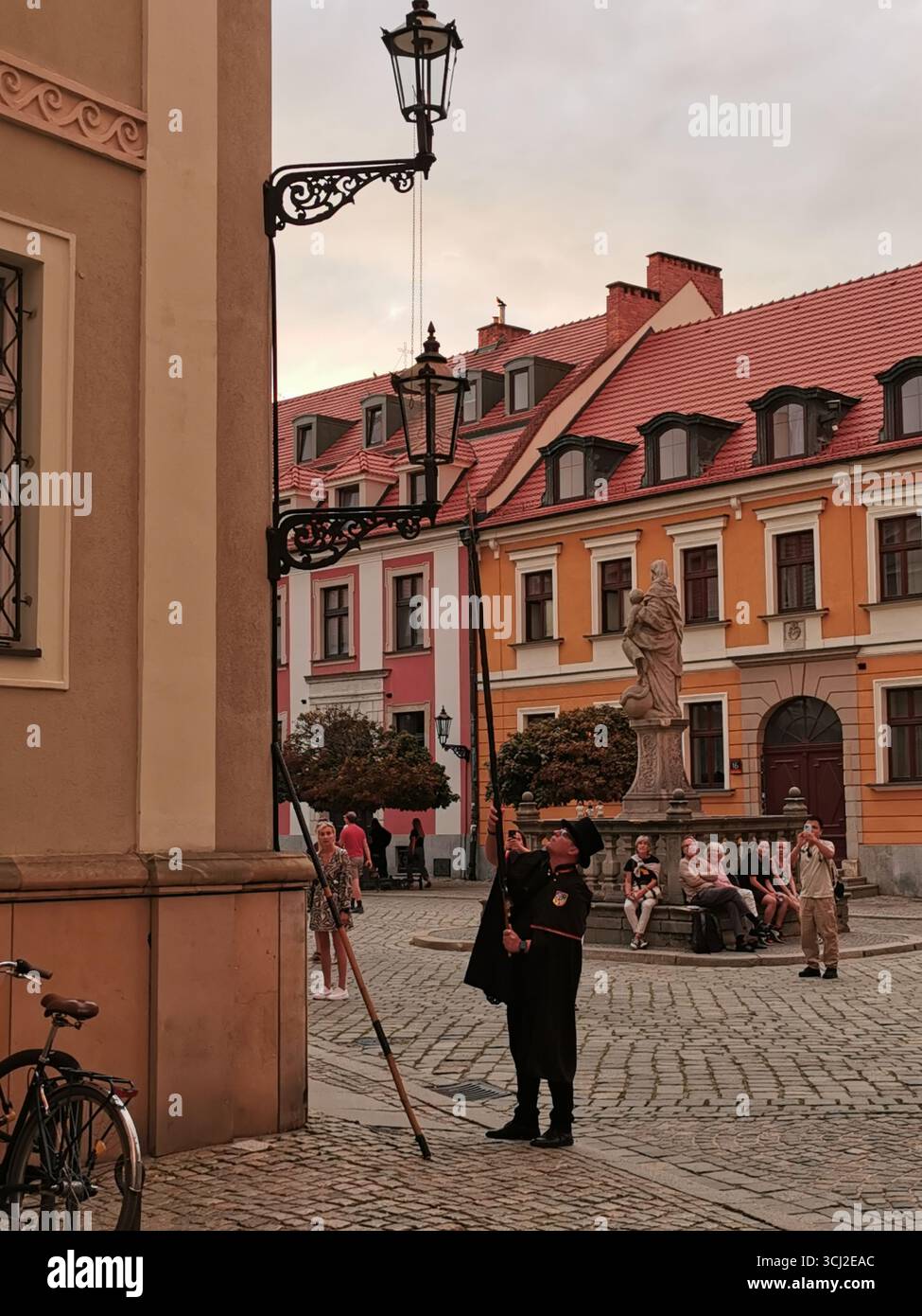Wrocław lamplighter in hat and cloak lighting gas lamps on Cathedral Island at dusk—historic tradition, Poland, tourism, street scene, Ostrów Tumski. - Smartphone Captured Stock Image