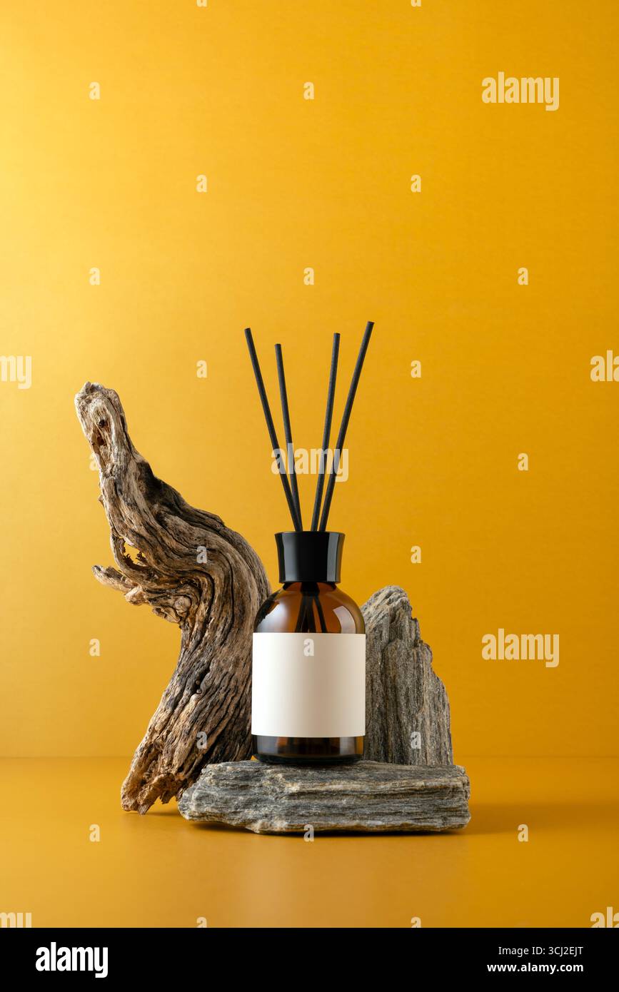 Aroma diffuser in brown glass bottle on stone podium with sticks, driftwood and on orange background, minimalist still life with natural textures and Stock Photo