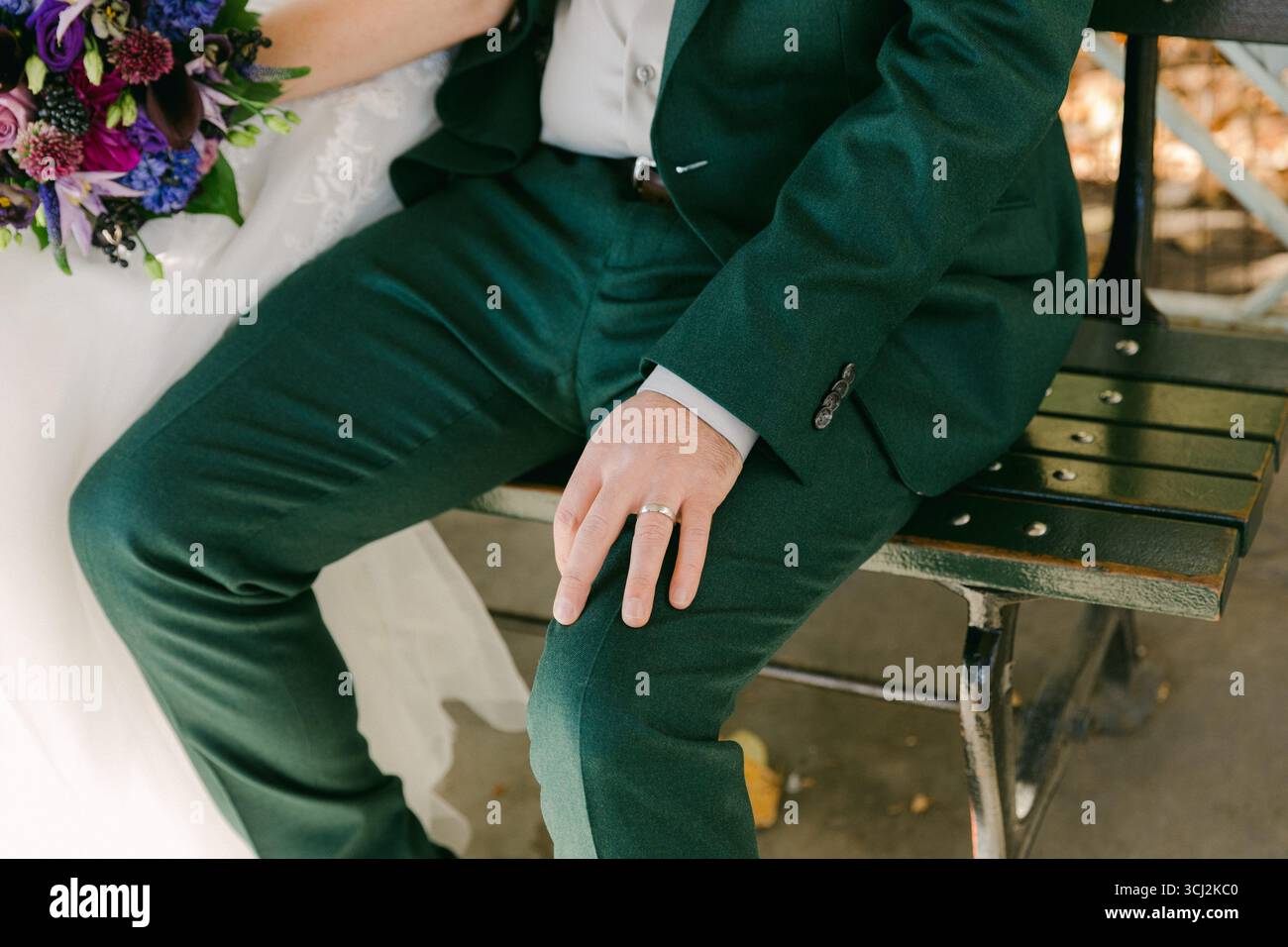 Couple sits closely on a park bench, celebrating their love with vibrant wedding attire and a beautiful bouquet nearby. Stock Photo