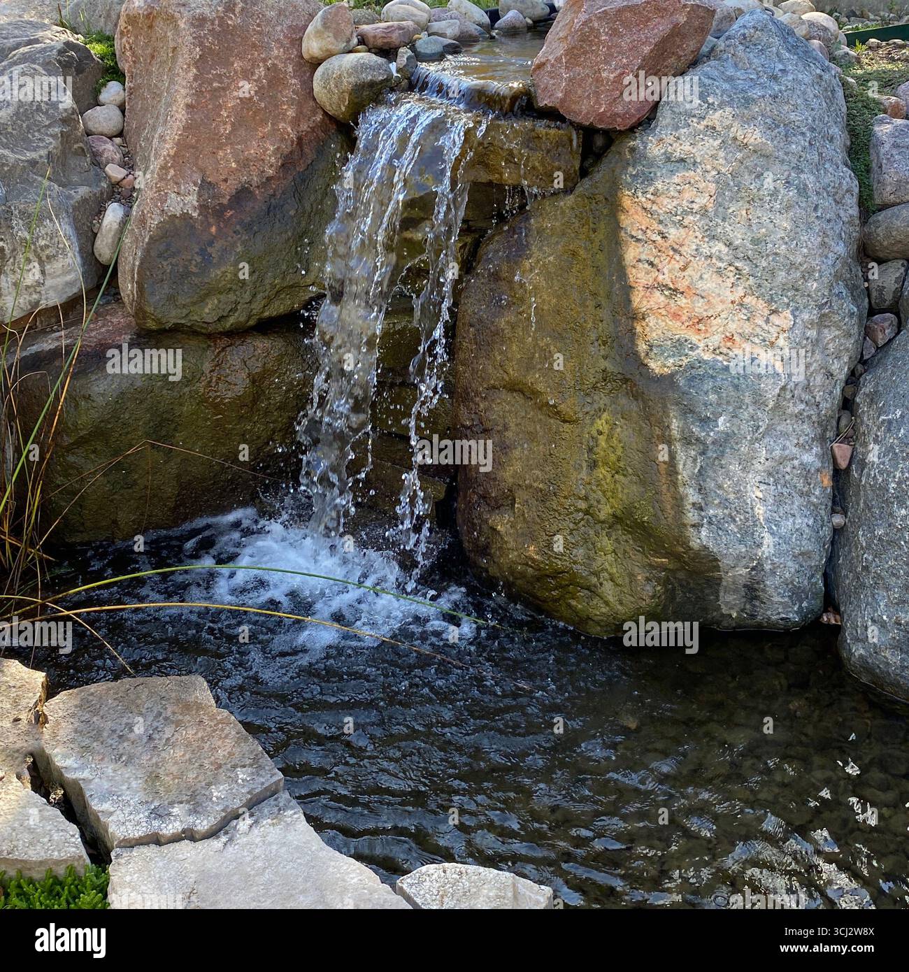 A small waterfall tumbling over boulders into a small pond at Sinnissippi Gardens in Rockford, Illinois, USA - Smartphone Captured Stock Image