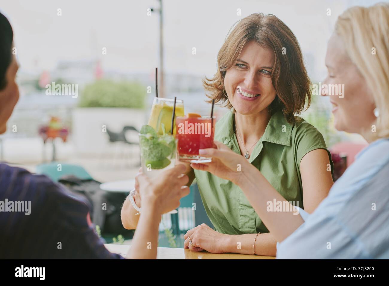 Middle Aged Women Smiling While Toasting Colorful Drinks Outdoors Stock Photo
