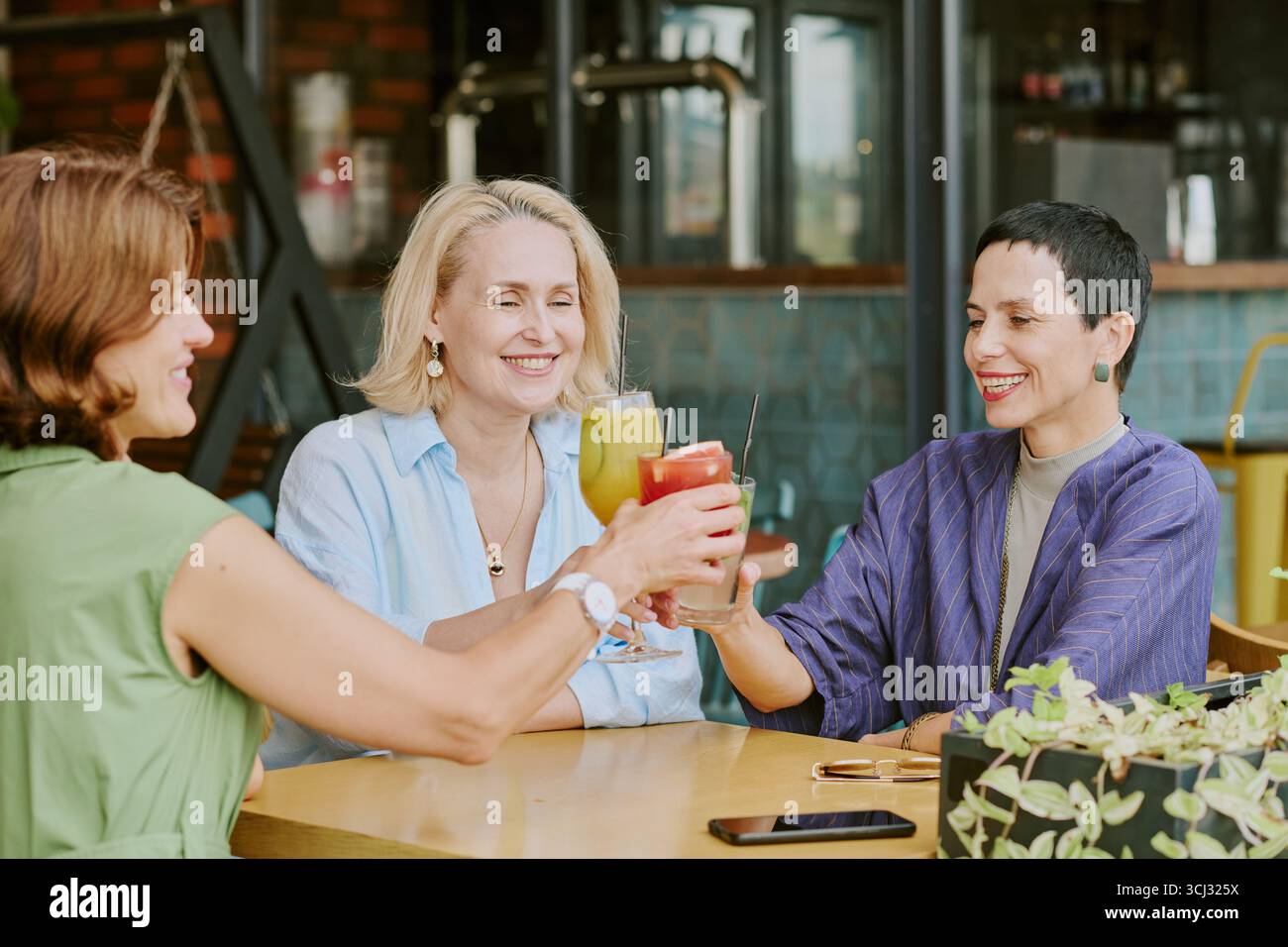 Three Middle Aged Women Smiling While Toasting with Cocktails Stock Photo
