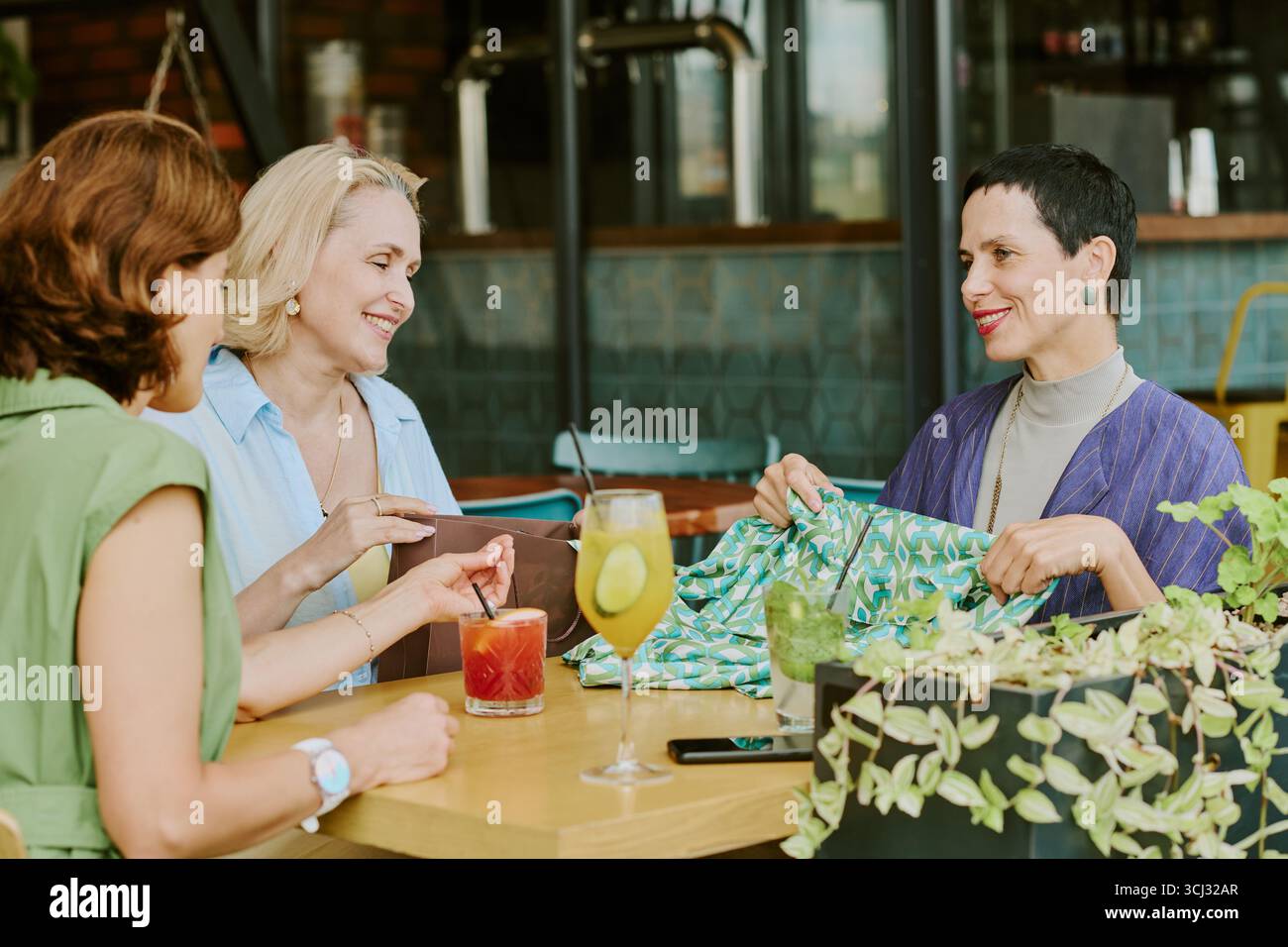 Three Middle Aged Women Socializing and Smiling at Restaurant Table Stock Photo
