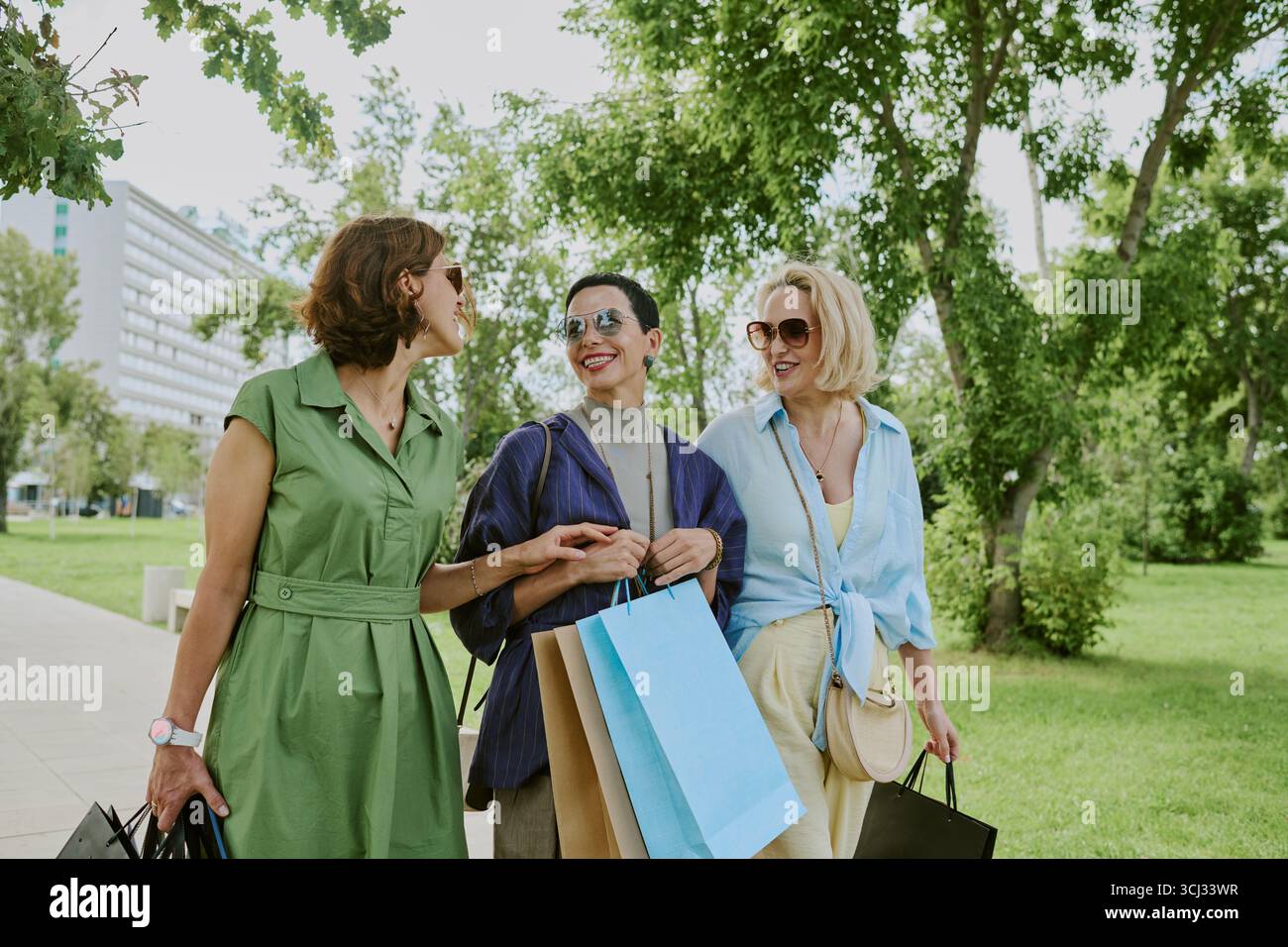 Three Middle Aged Women Chatting While Walking Outdoors with Bags Stock Photo