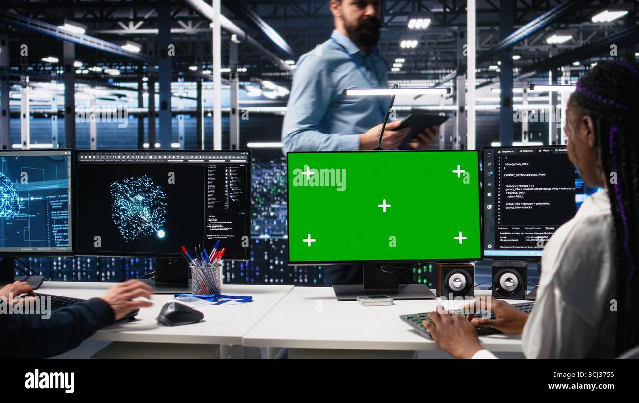 Data center engineers managing AI systems for uptime and efficiency using chroma key PC. Teamworking IT specialists using artificial intelligence on green screen computer in server hub, camera A Stock Photo