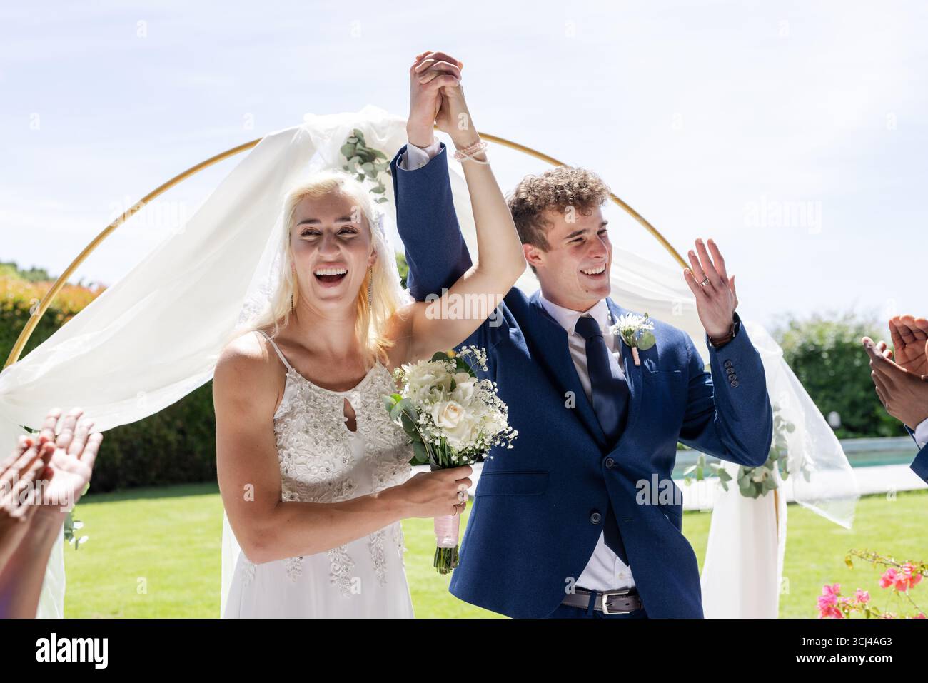 Bride and groom celebrating outdoors, holding hands and smiling joyfully Stock Photo