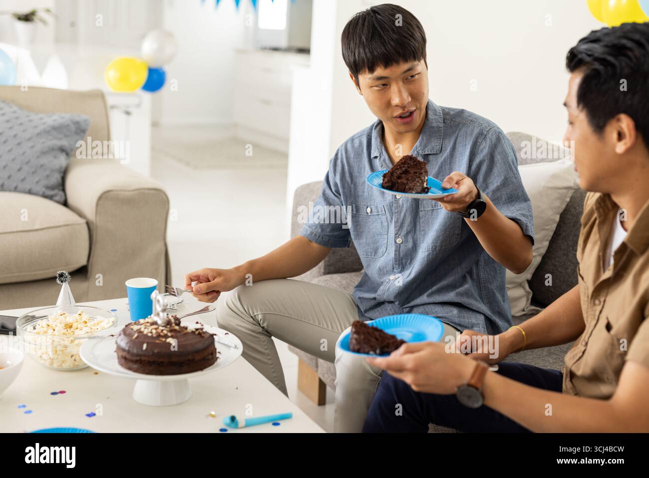 Friends enjoying chocolate cake and conversation at home during casual gathering Stock Photo