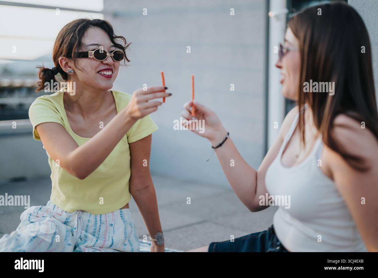 Young women enjoying a snack and laughing during a rooftop hangout Stock Photo