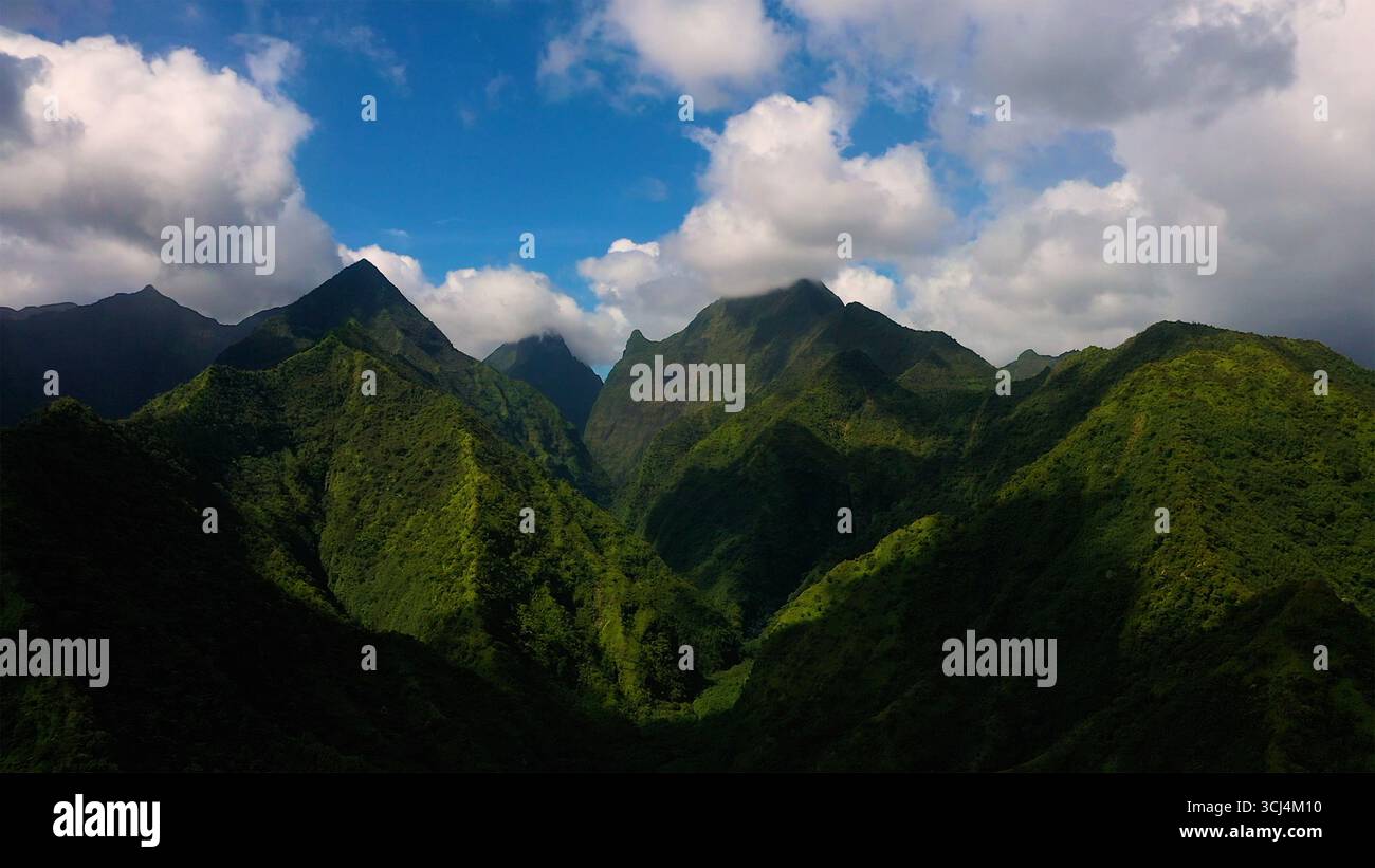 Aerial view of dramatic, lush green mountains under a bright sky dotted ...