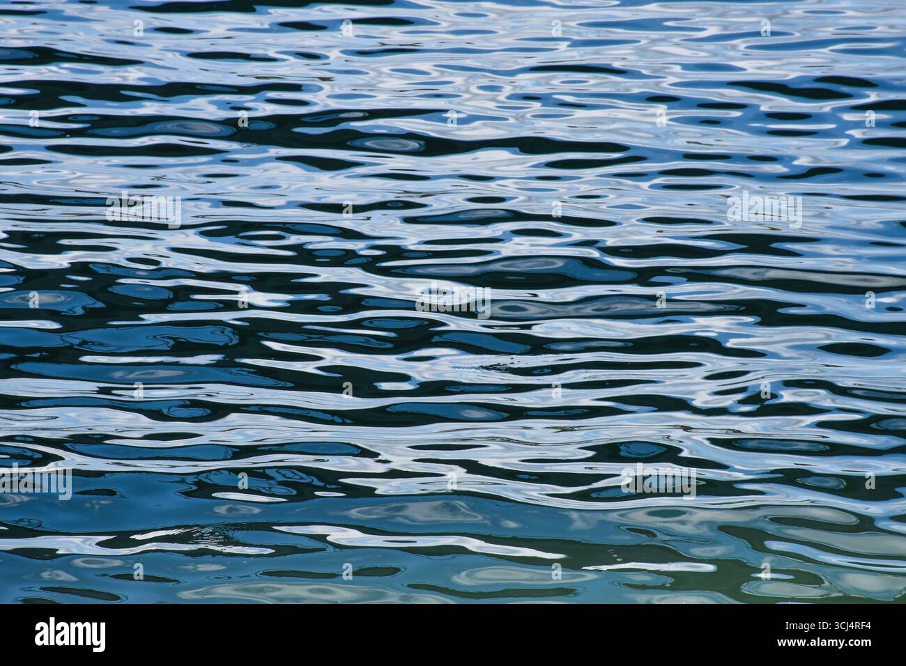 Daytime sky reflected on calm river water with soft ripples, forming abstract natural textures without visible land or shore. Stock Photo