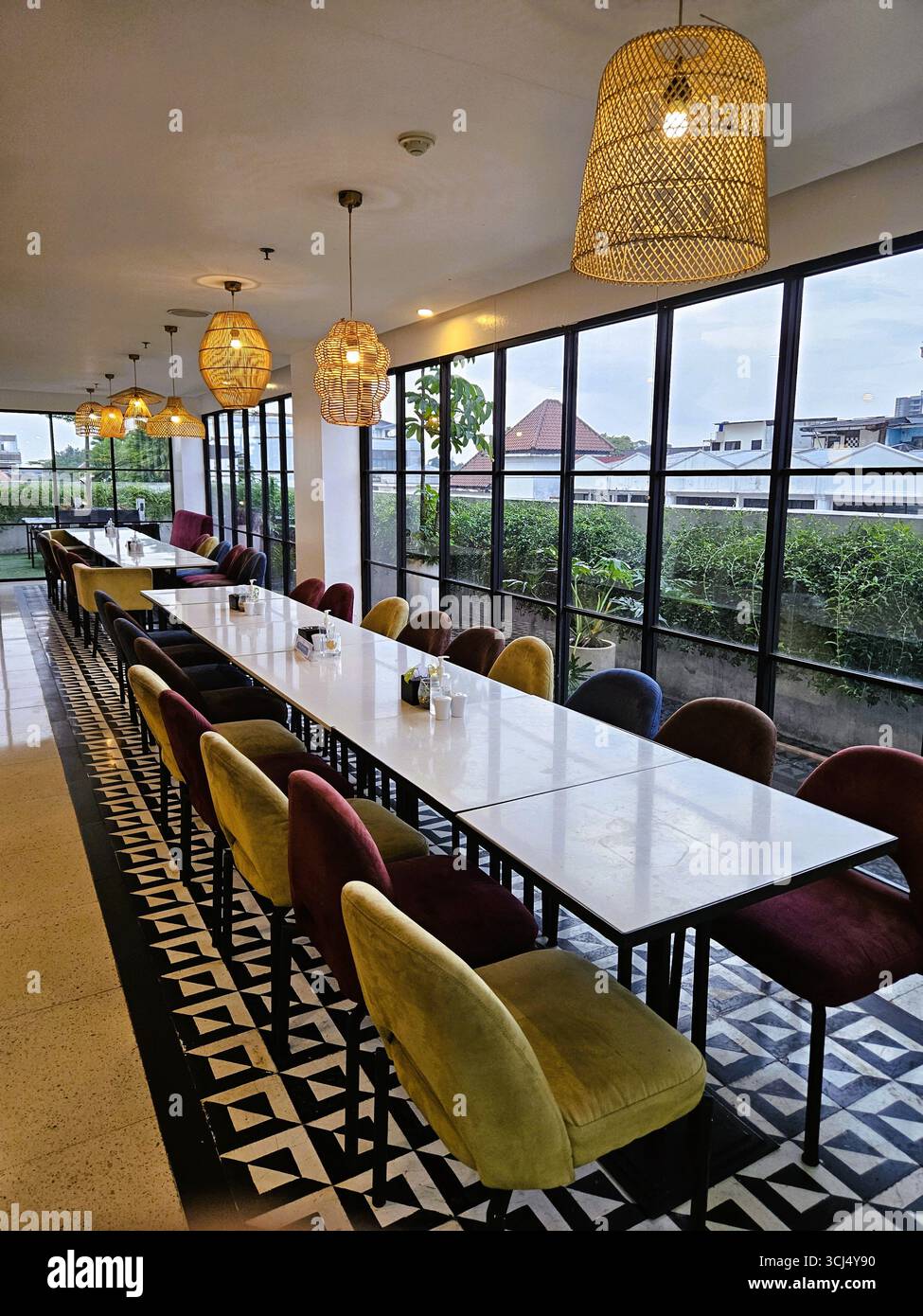 Modern cafe interior with long table, colorful chairs, and warm lighting design. Bandung, Indonesia - March 28th, 2024 - Smartphone Captured Stock Image