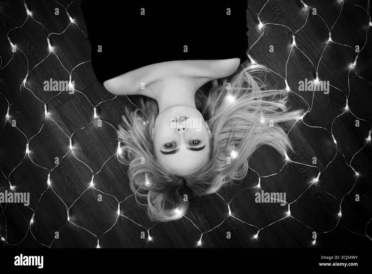 Beautiful girl lying on floor with christmas lights, monochrome Stock Photo