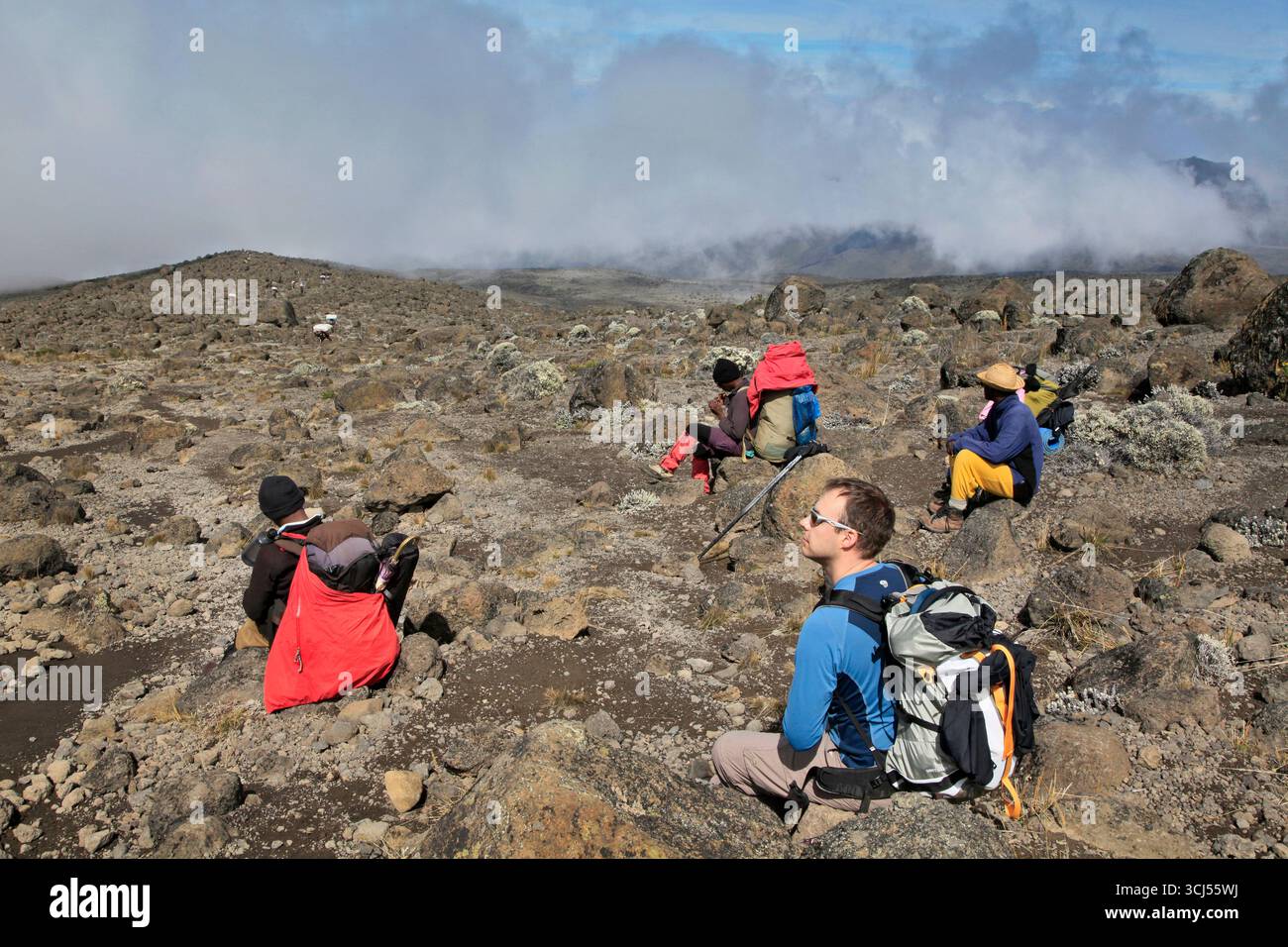 Hiker and local guides resting, along Machame Route of Mt. Kilimanjaro. Stock Photo