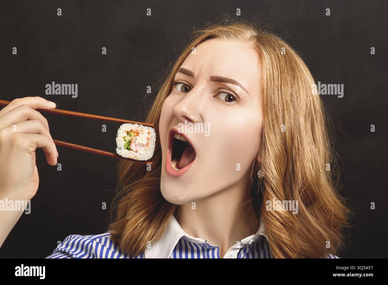 Fun young woman eating sushi on black background Stock Photo