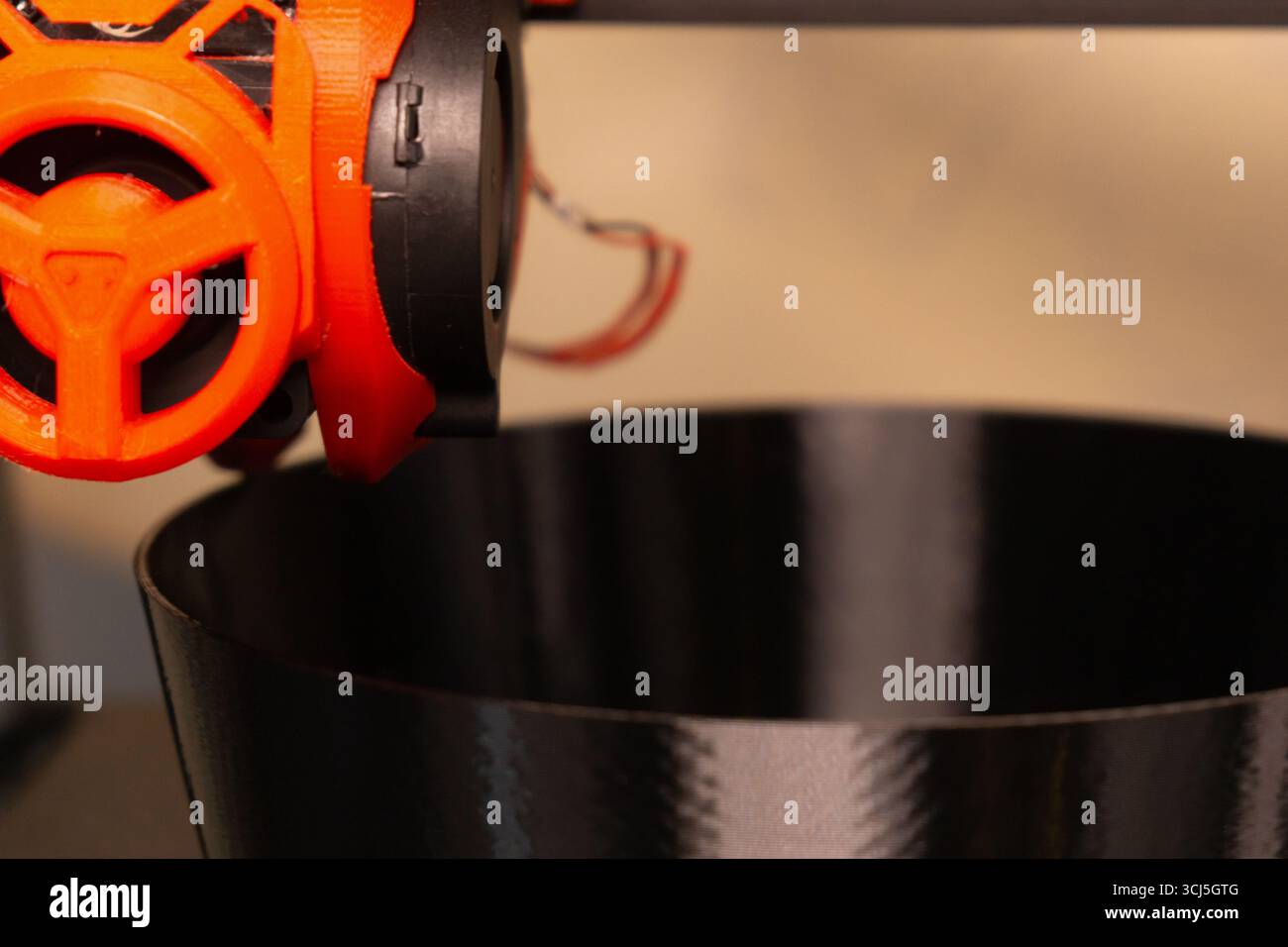 A 3D printer is poised above a dark, glossy bowl, showcasing advanced technology in action. The printer's nozzle and extruder hint at the innovative d Stock Photo